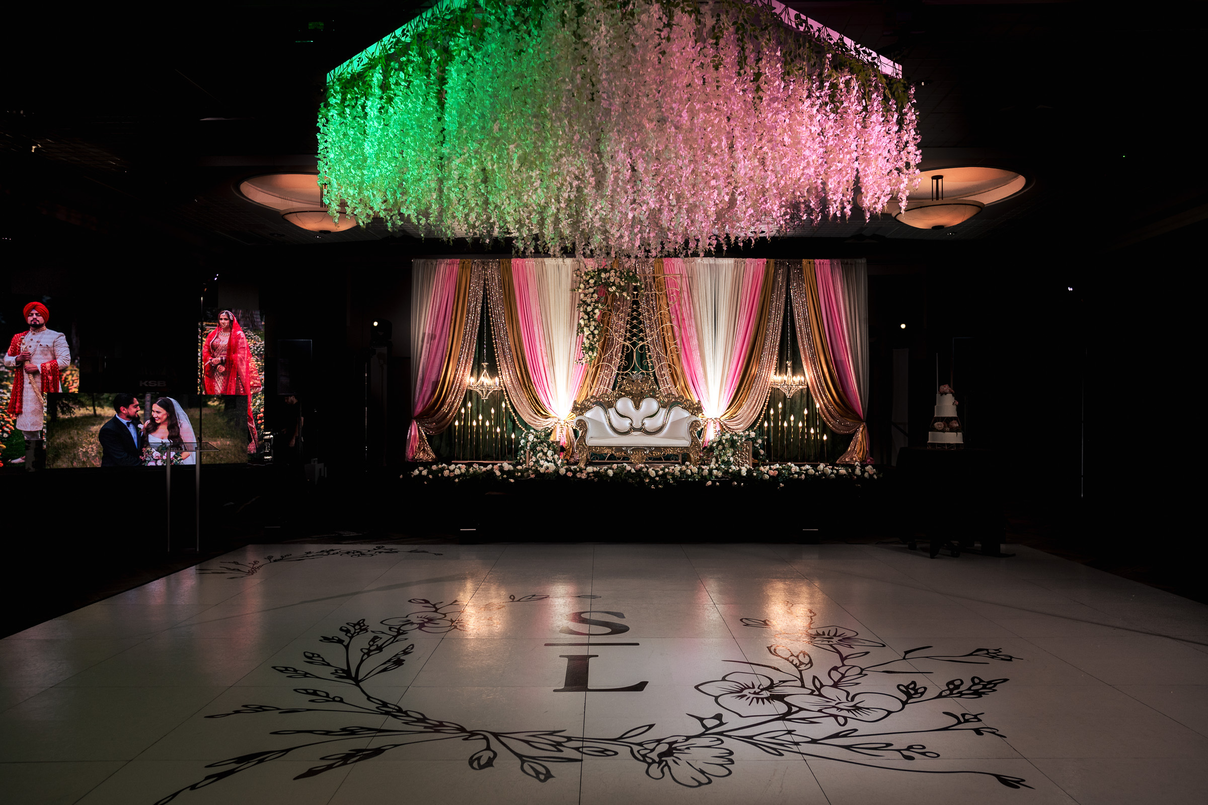 Lavish decorated wedding stage with floral ceiling and illuminated drapes.