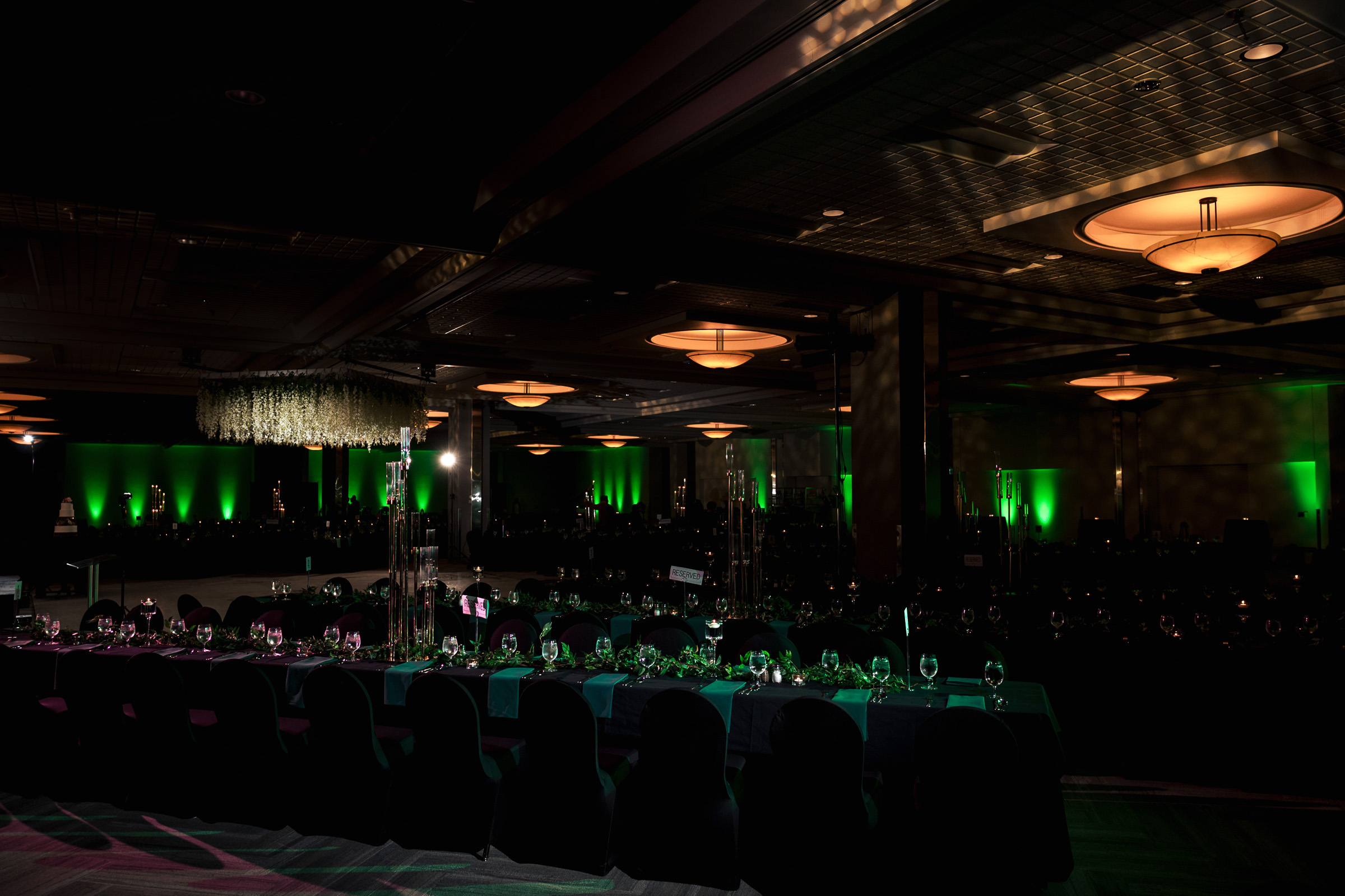 Dimly lit banquet hall with green ambient lighting and tables set for an event.