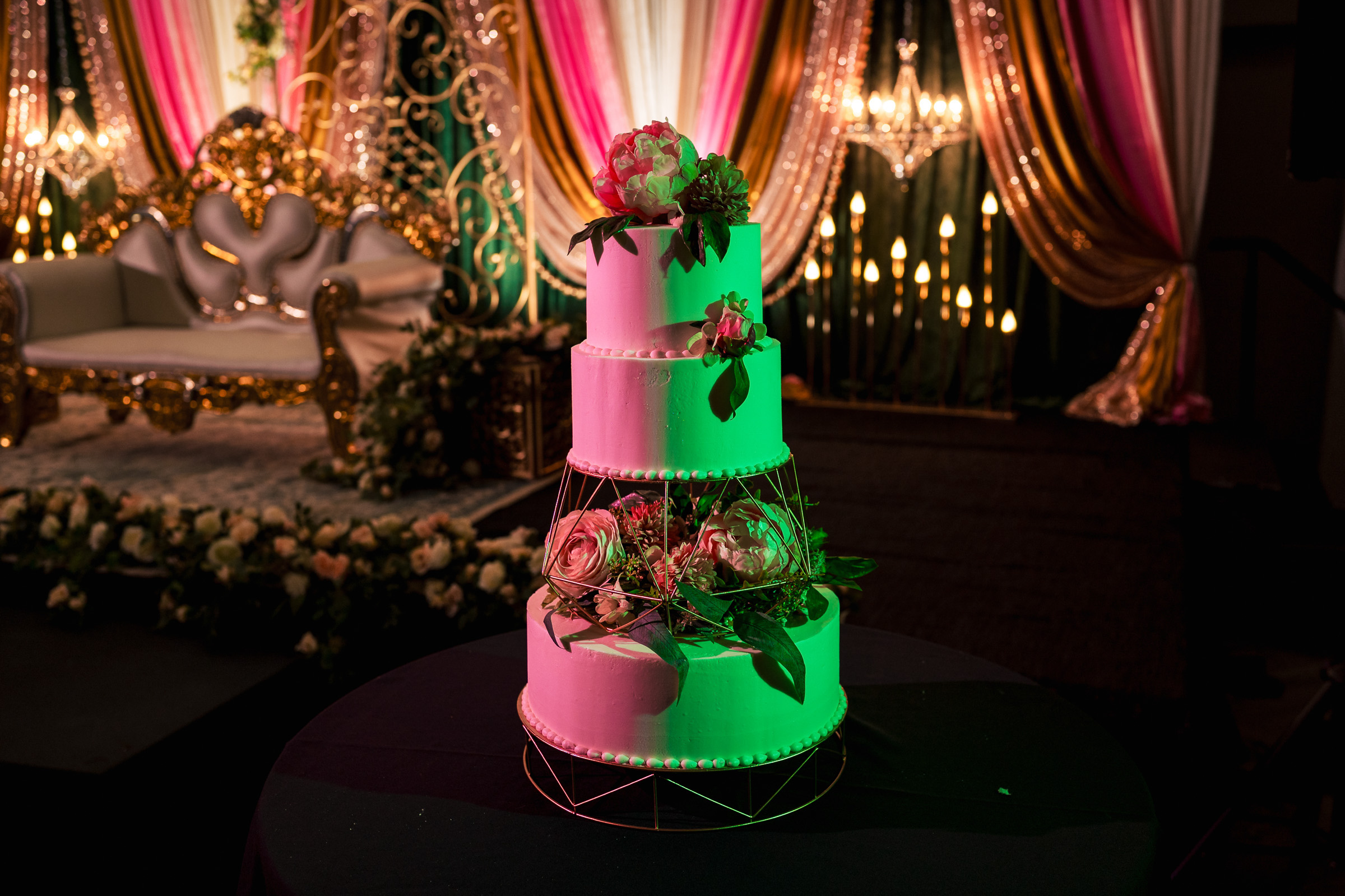 Three-tiered wedding cake with floral decorations, set against a vibrant, draped backdrop.