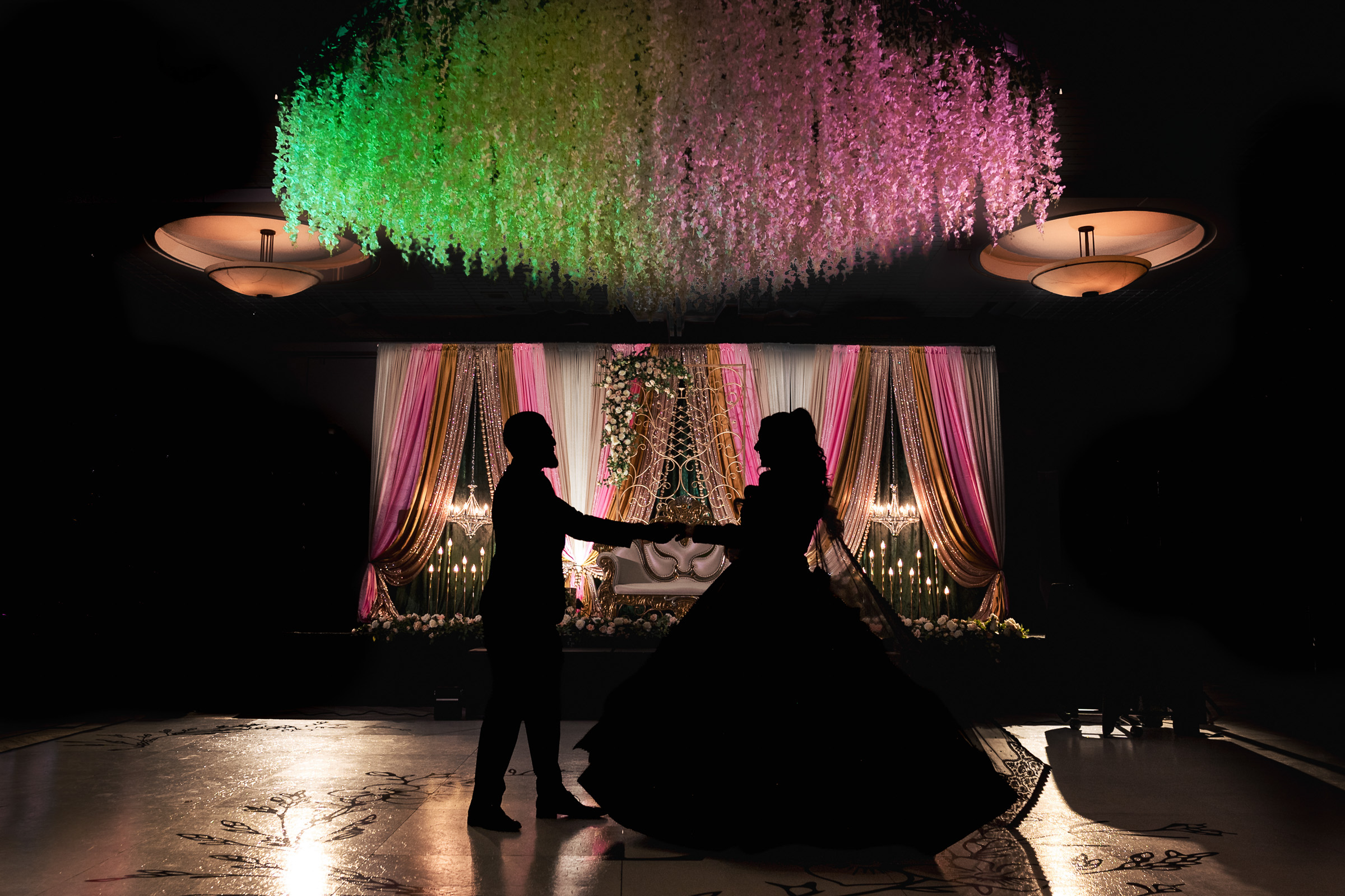 Silhouette of a couple dancing under vibrant floral ceiling decorations at an event.