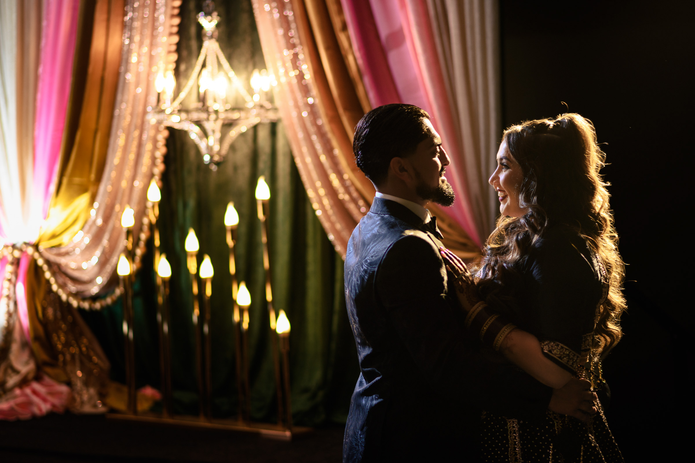A couple dancing in dim lighting with draped fabric and candles in the background.