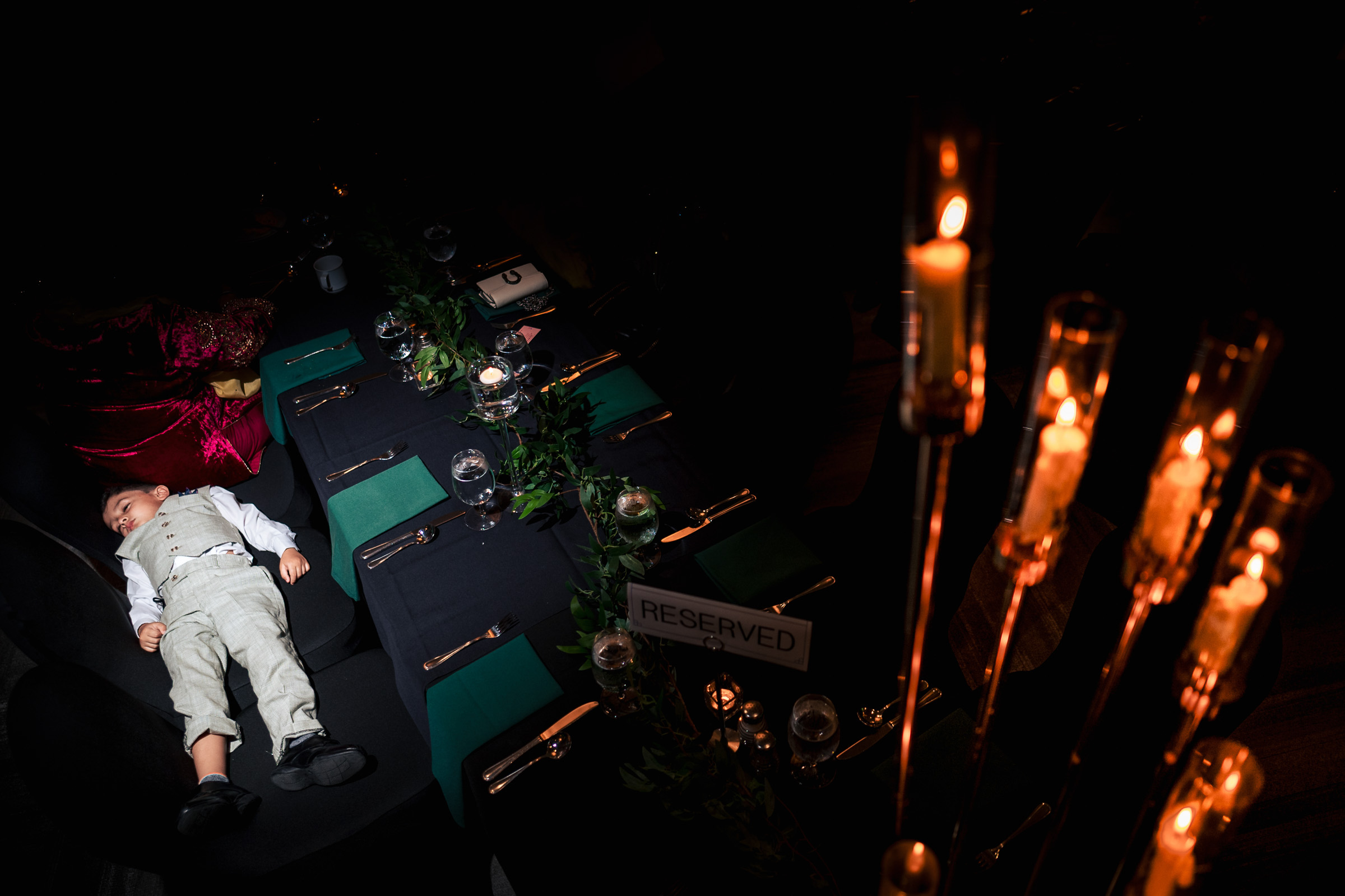 Child sleeping on a chair at a dimly lit, elegantly set dinner table.