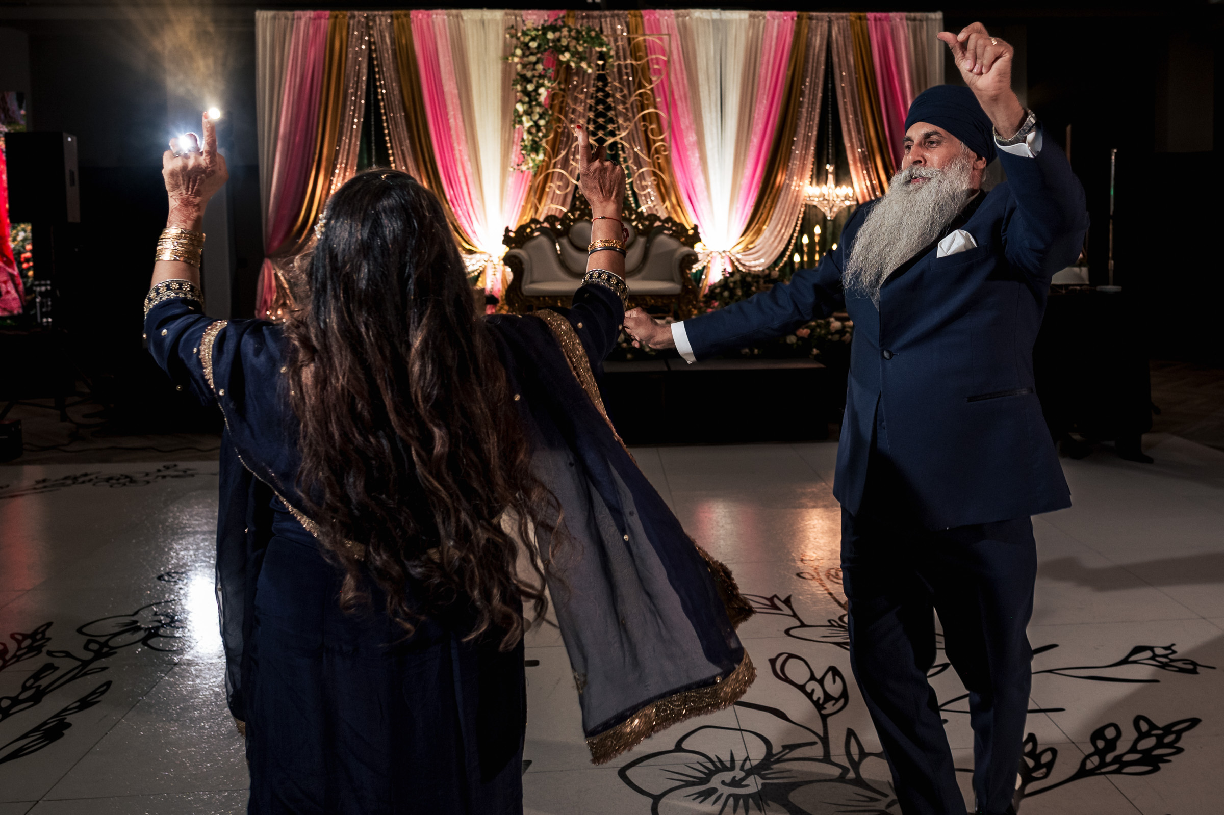 Two people dancing joyfully at a decorated event with colorful drapes and lights.