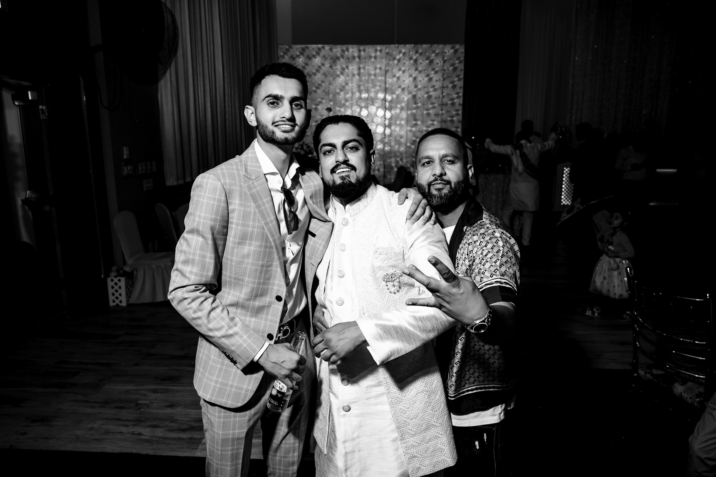 Three men in formal attire pose for a photo in a dimly lit event space.