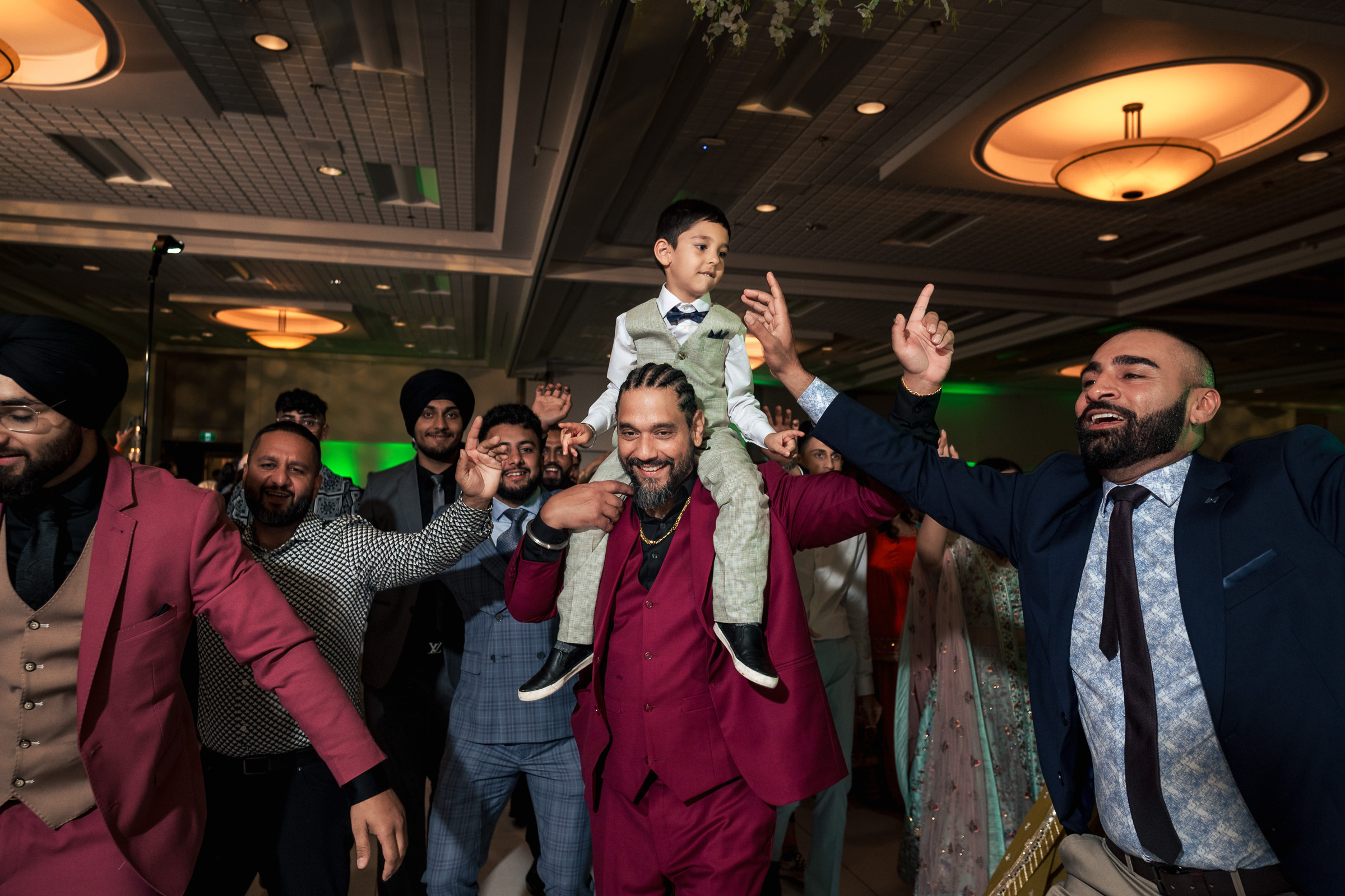 Group of people dancing at a formal event; man carries a boy on his shoulders.
