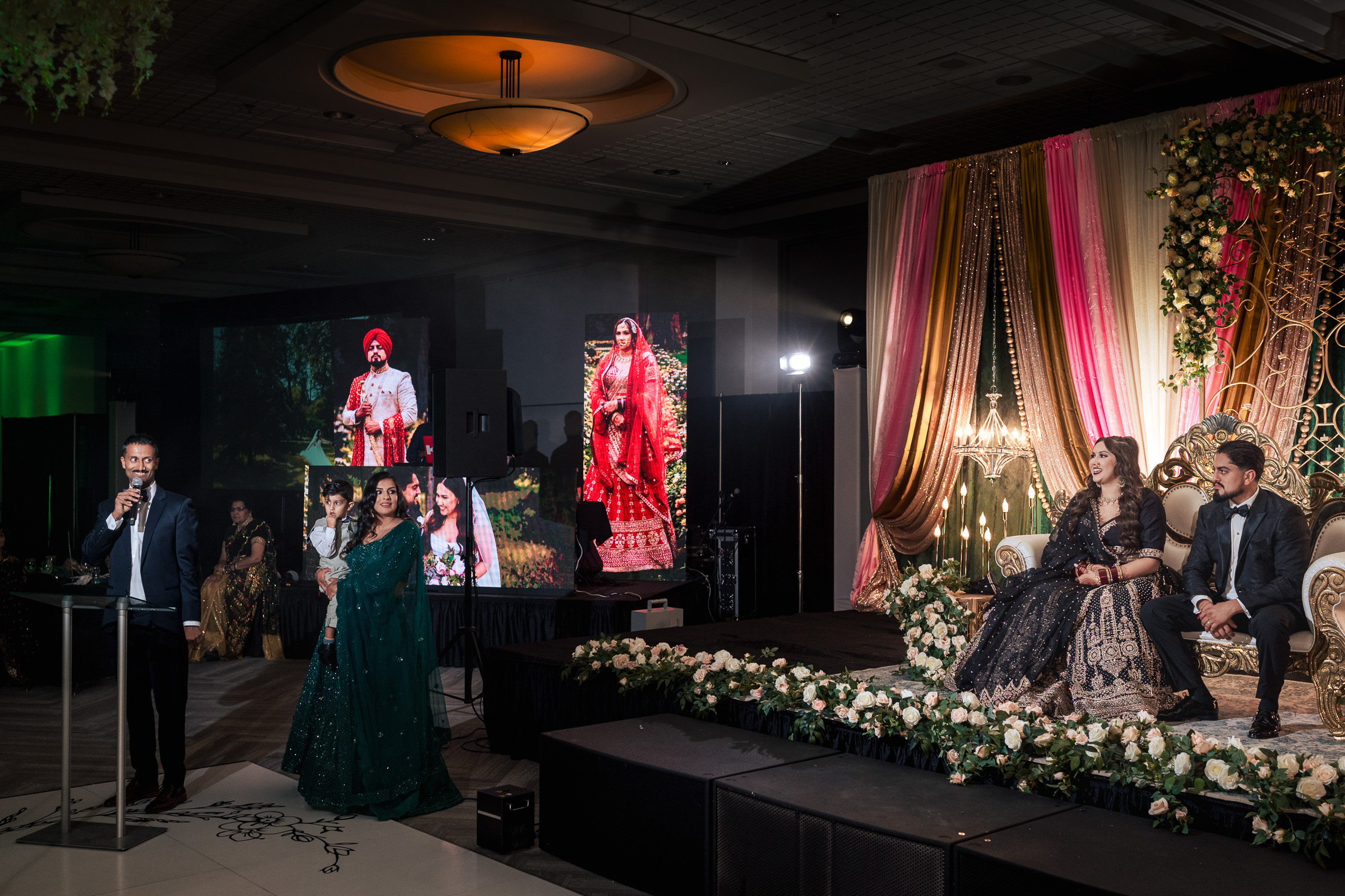 People at a formal event with speeches and a decorative stage in the background.