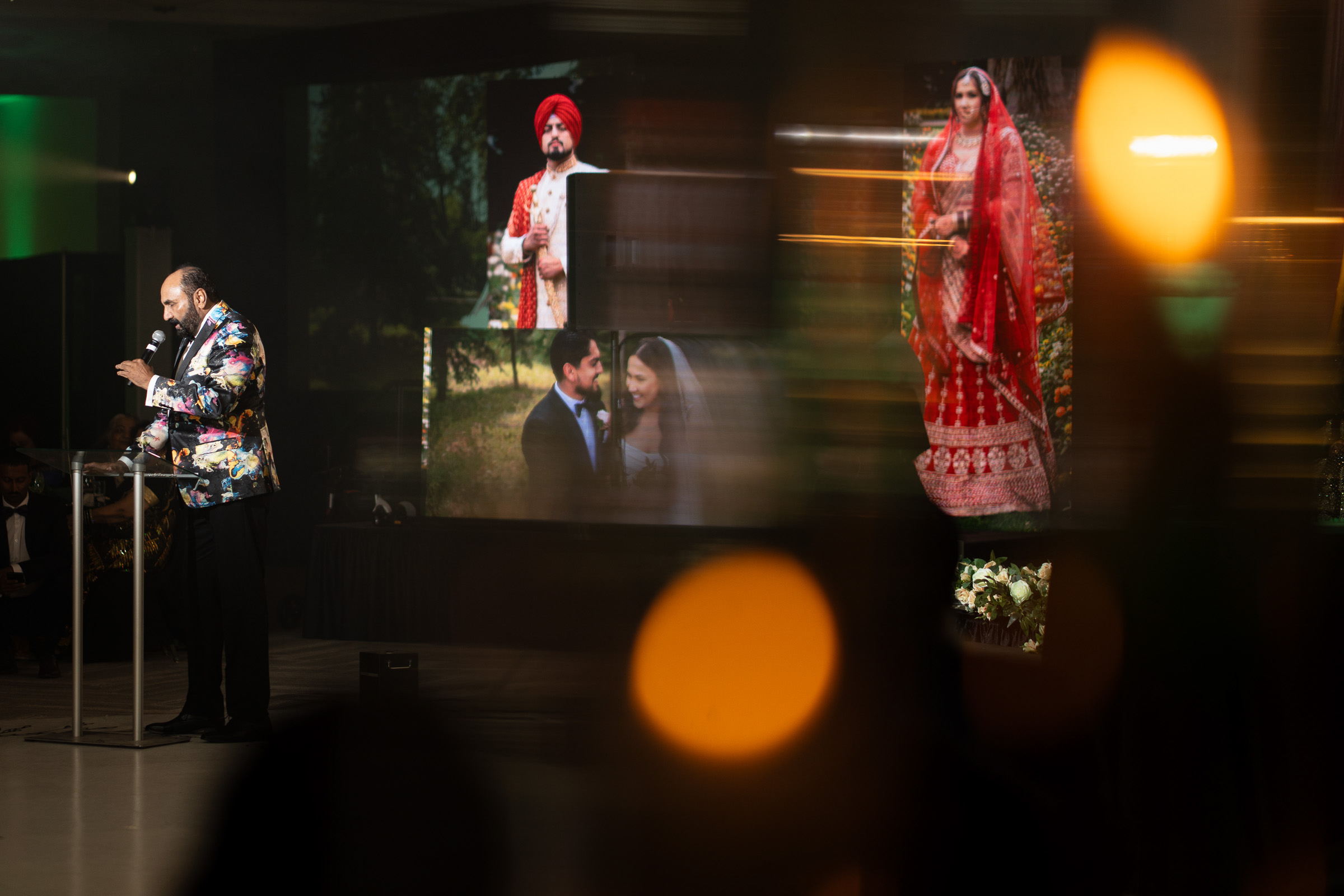 Person speaking on stage with wedding photos projected in the background.