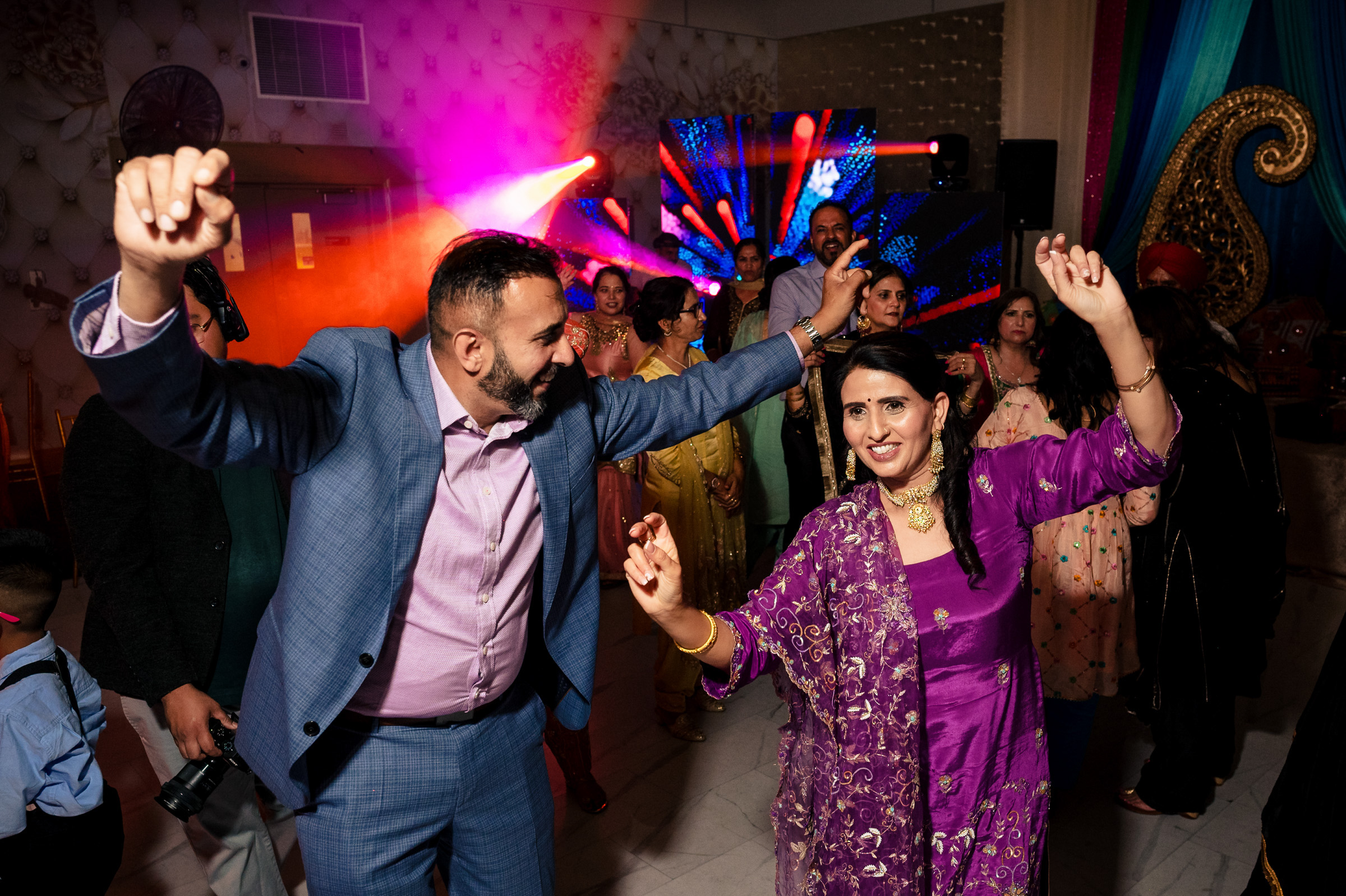 People dancing joyfully in colorful outfits at a lively indoor celebration.