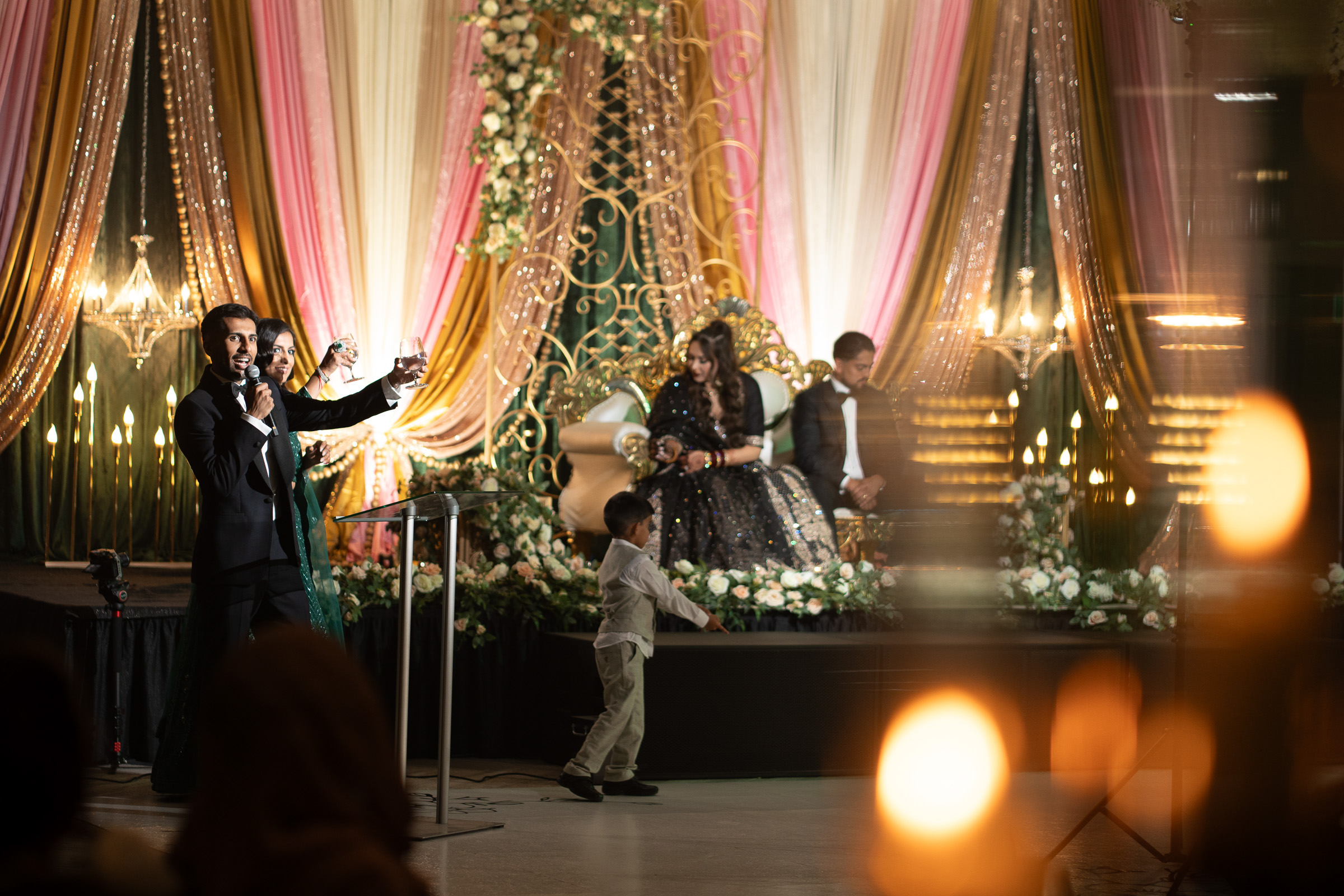 People on stage at an ornate event with draped decorations and soft lighting.