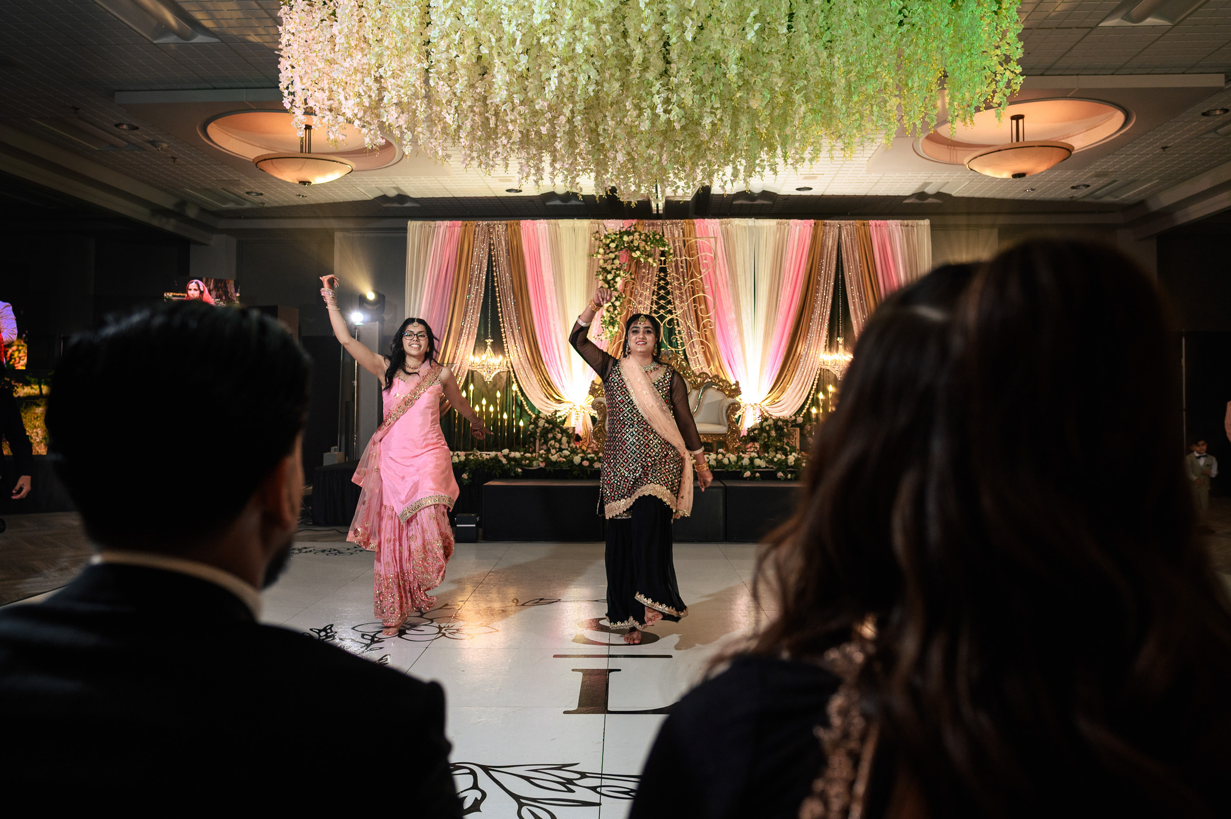Two women perform a dance at an indoor event, with an audience watching.