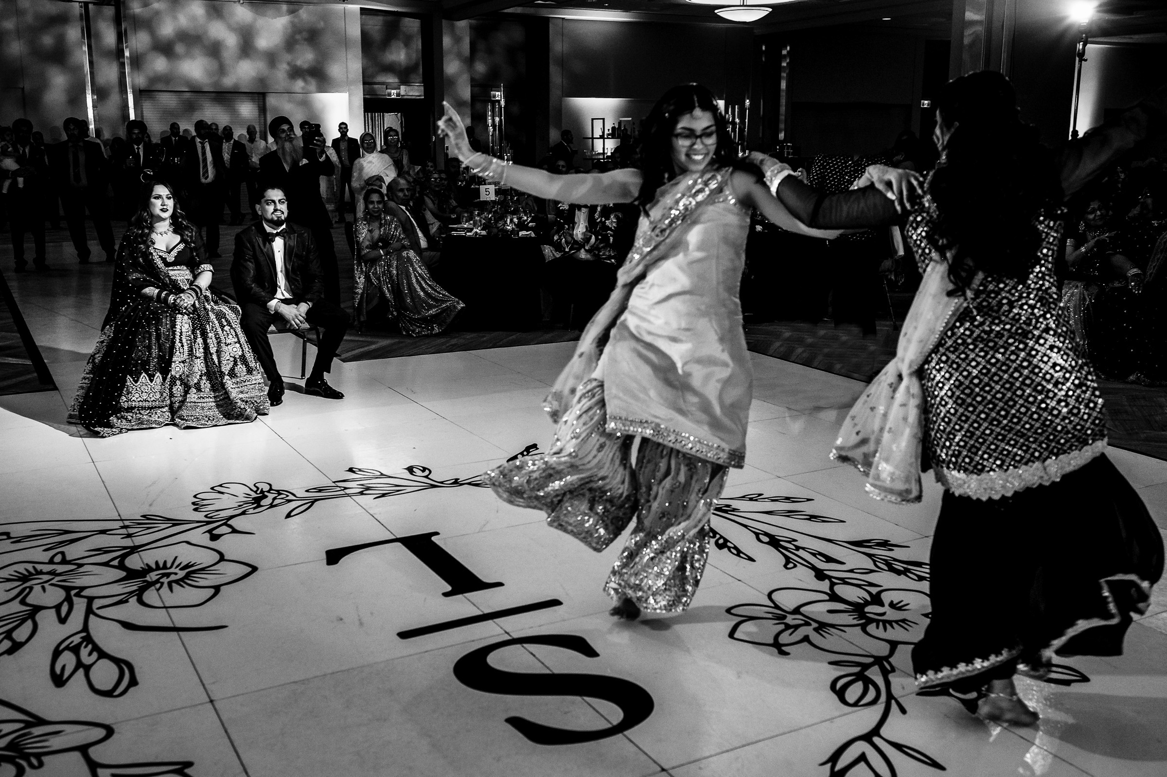 Women dancing energetically on a decorated floor with seated guests watching.
