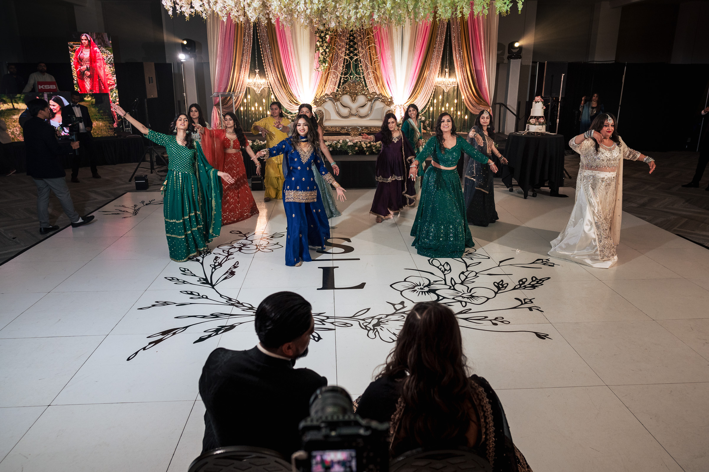 Group of people dancing at a decorated indoor event with floral designs on the floor.