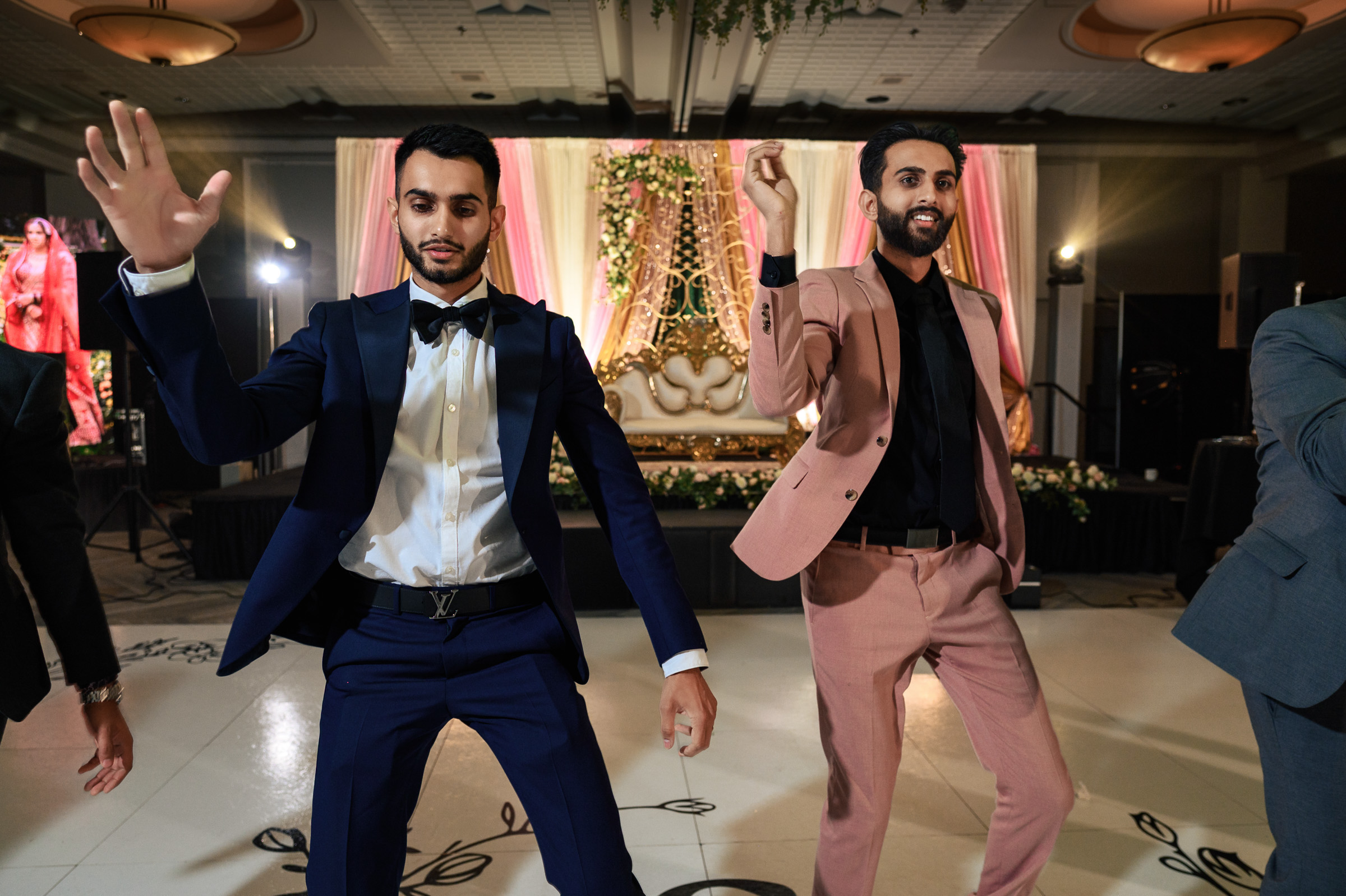Two men in suits dancing at an indoor event with a decorated backdrop.