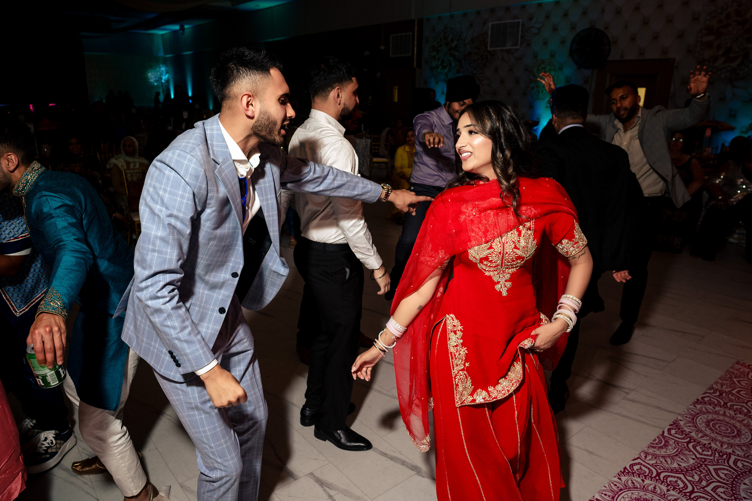 People dancing at a party; a woman in red and a man in a blue suit are smiling.