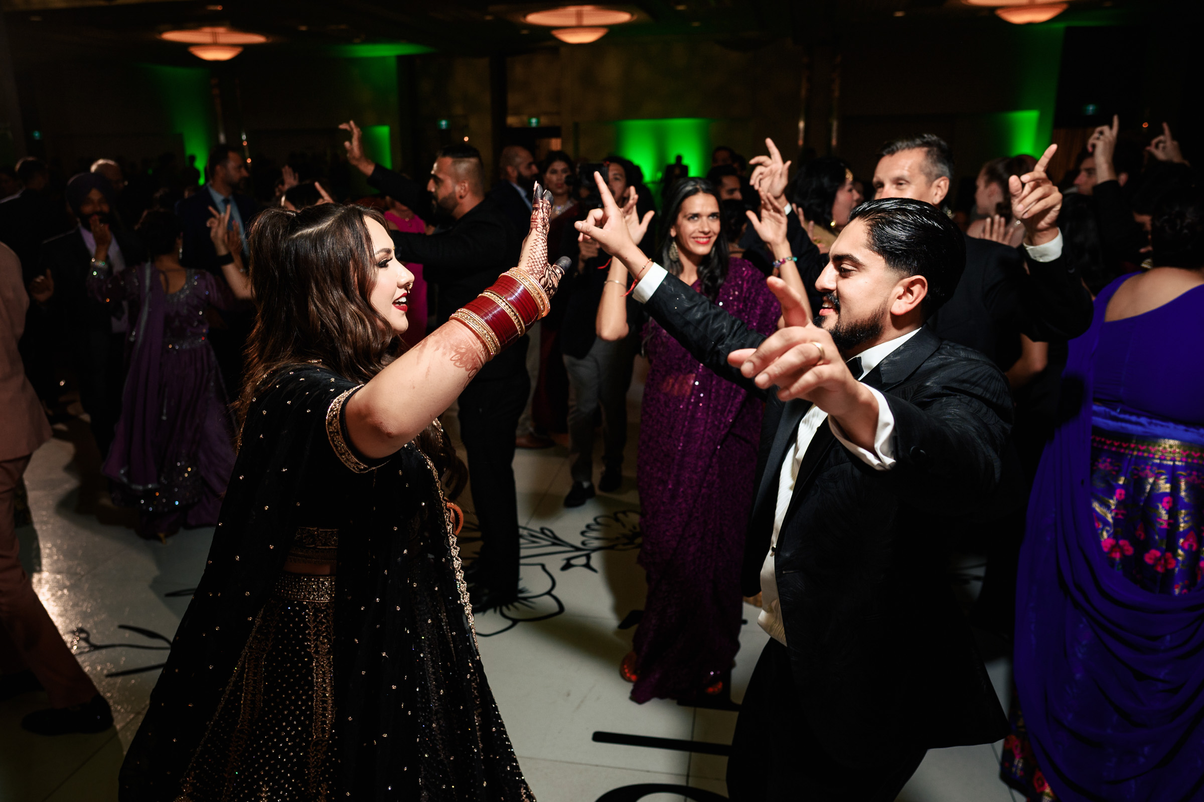 People dancing enthusiastically at an indoor party with green lighting.