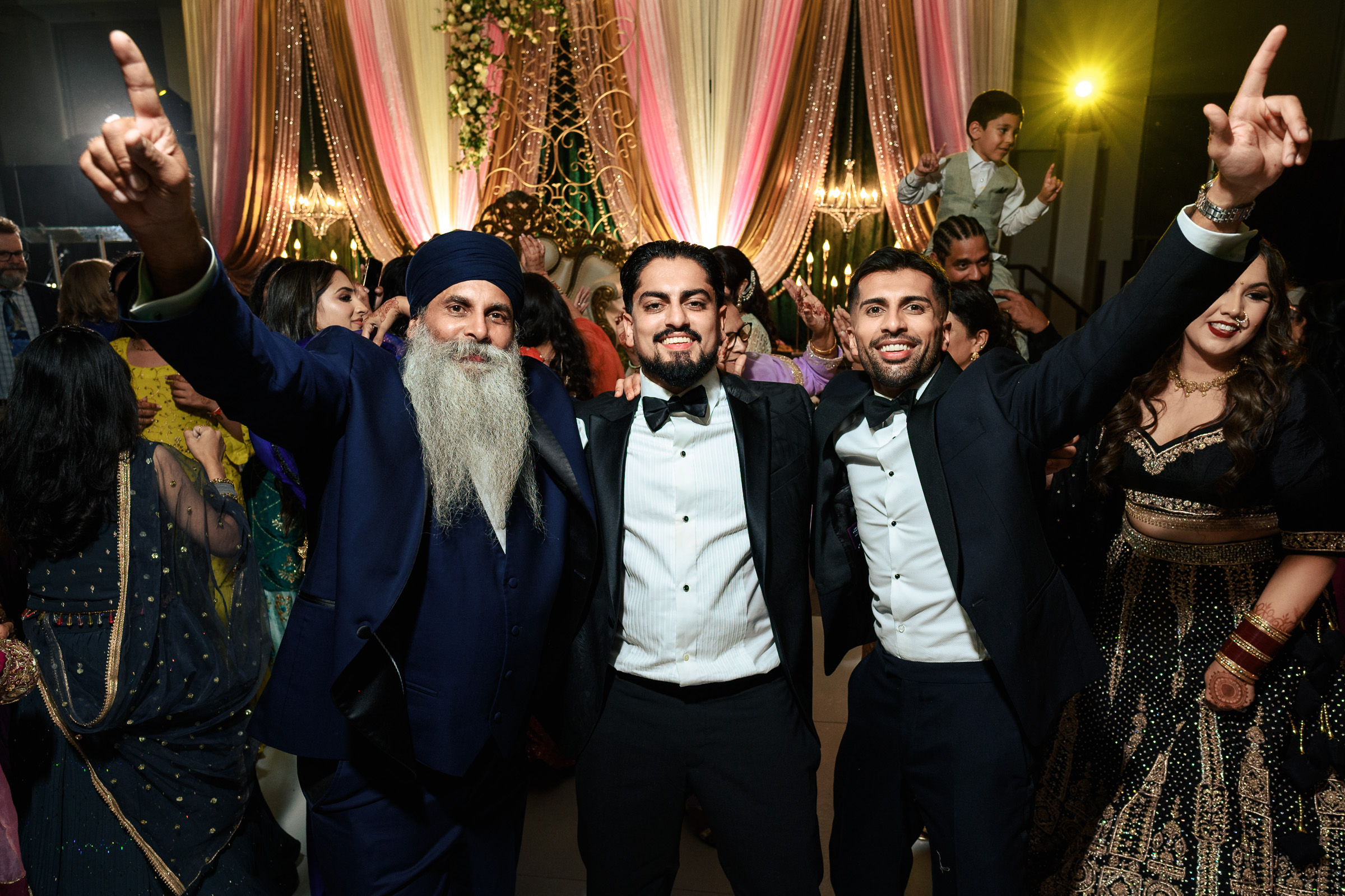 Three men in formal attire celebrating at an indoor event with colorful drapes.