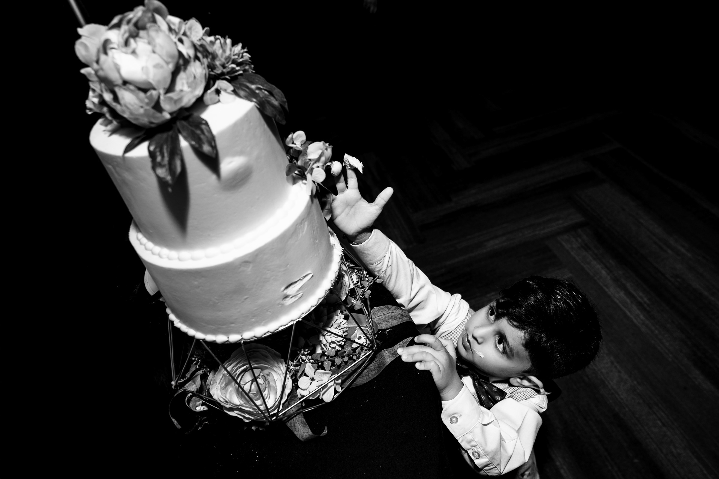 Child reaching for a two-tiered cake decorated with flowers on a stand.