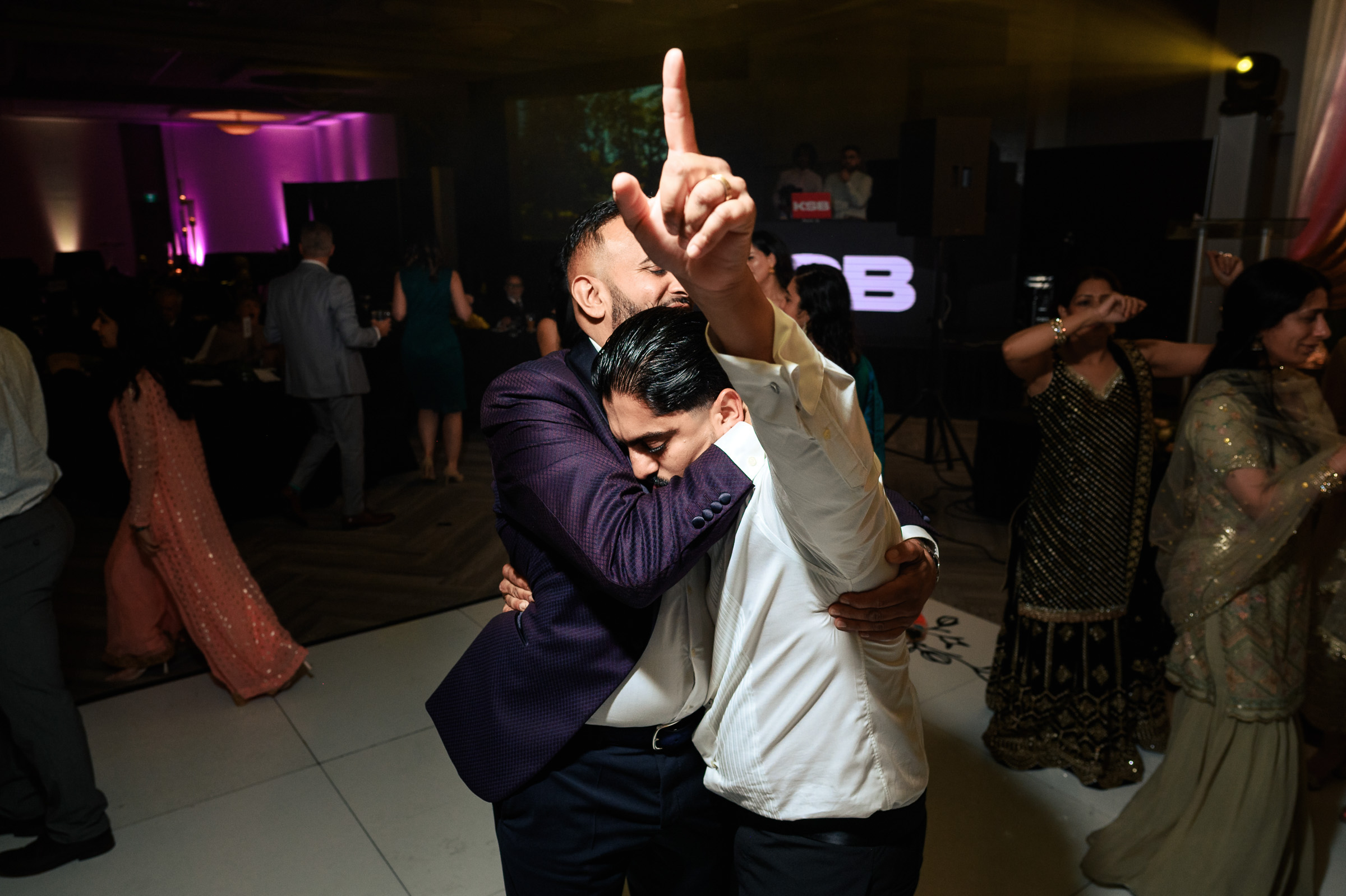 Two men hug and dance at an event, with one pointing upward enthusiastically.