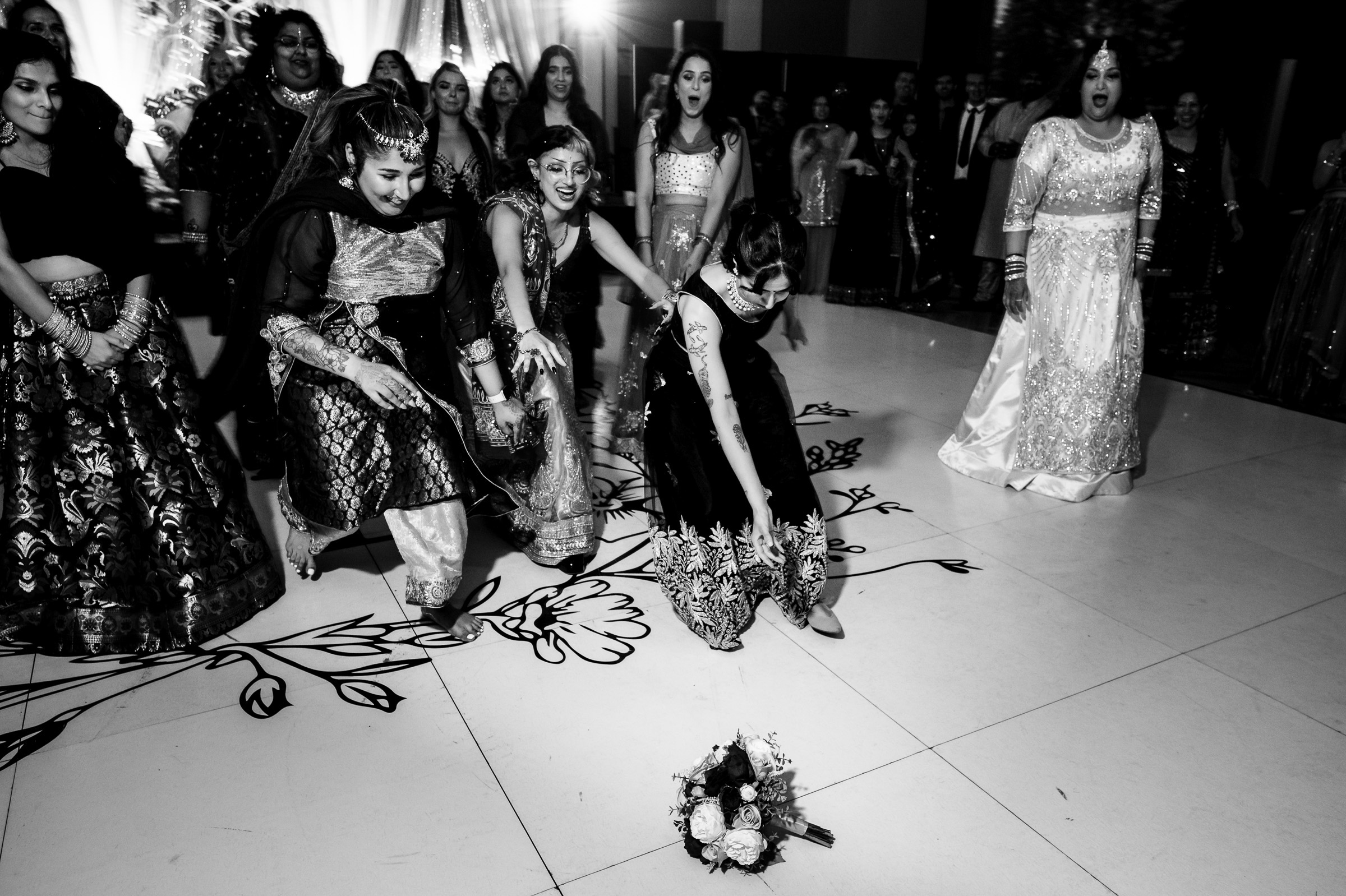 Women in traditional attire at a wedding catching a bouquet on the dance floor.