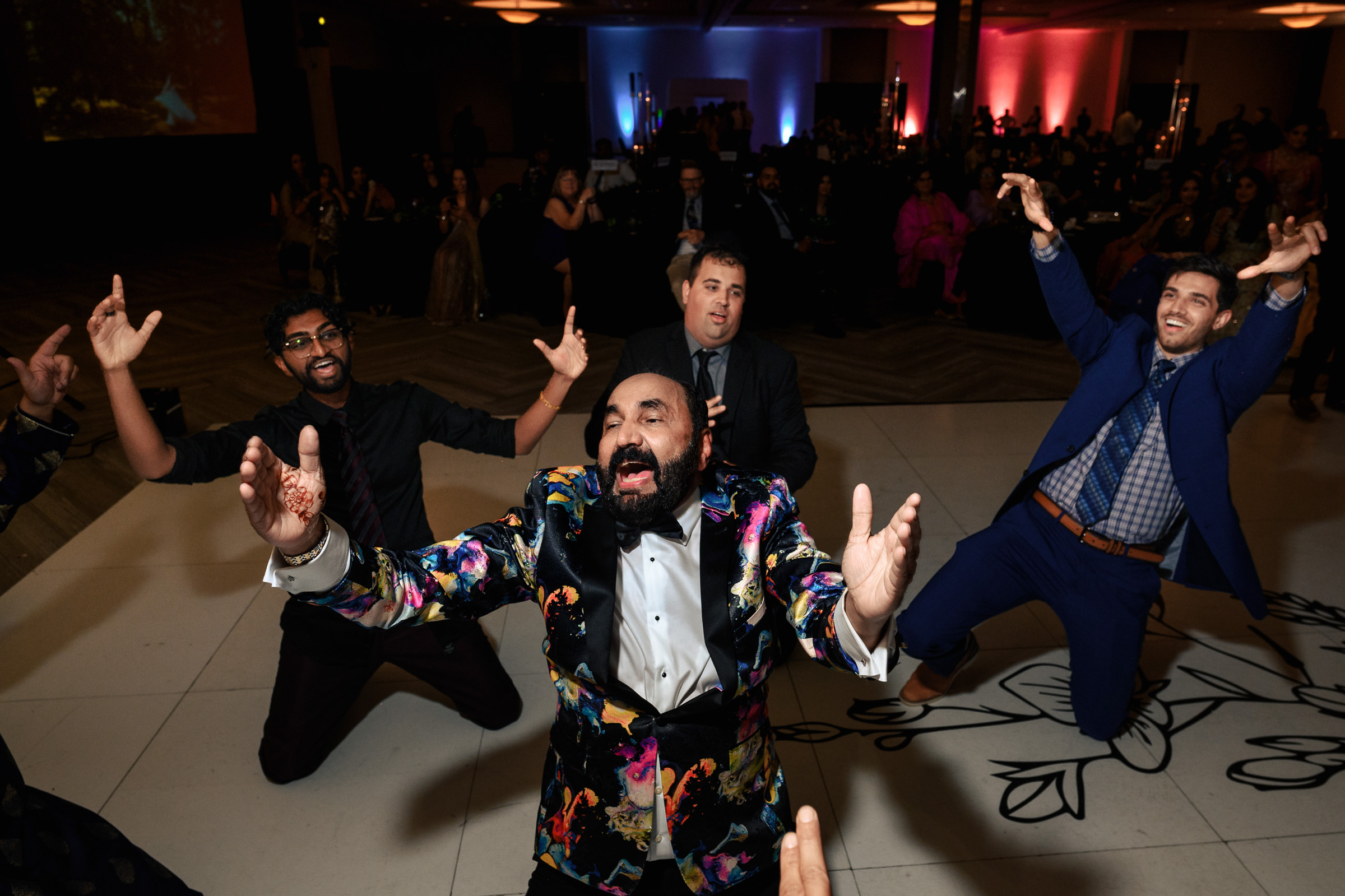 People dancing energetically at an indoor event, with colorful lighting in the background.