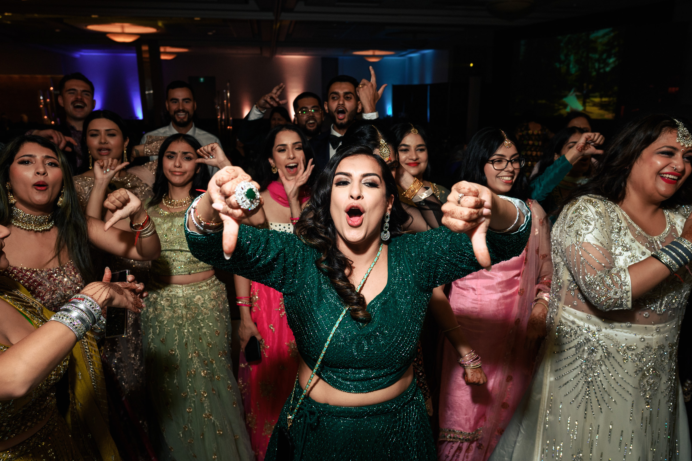 People at a lively party indoors, one woman gesturing thumbs down, all wearing festive attire.