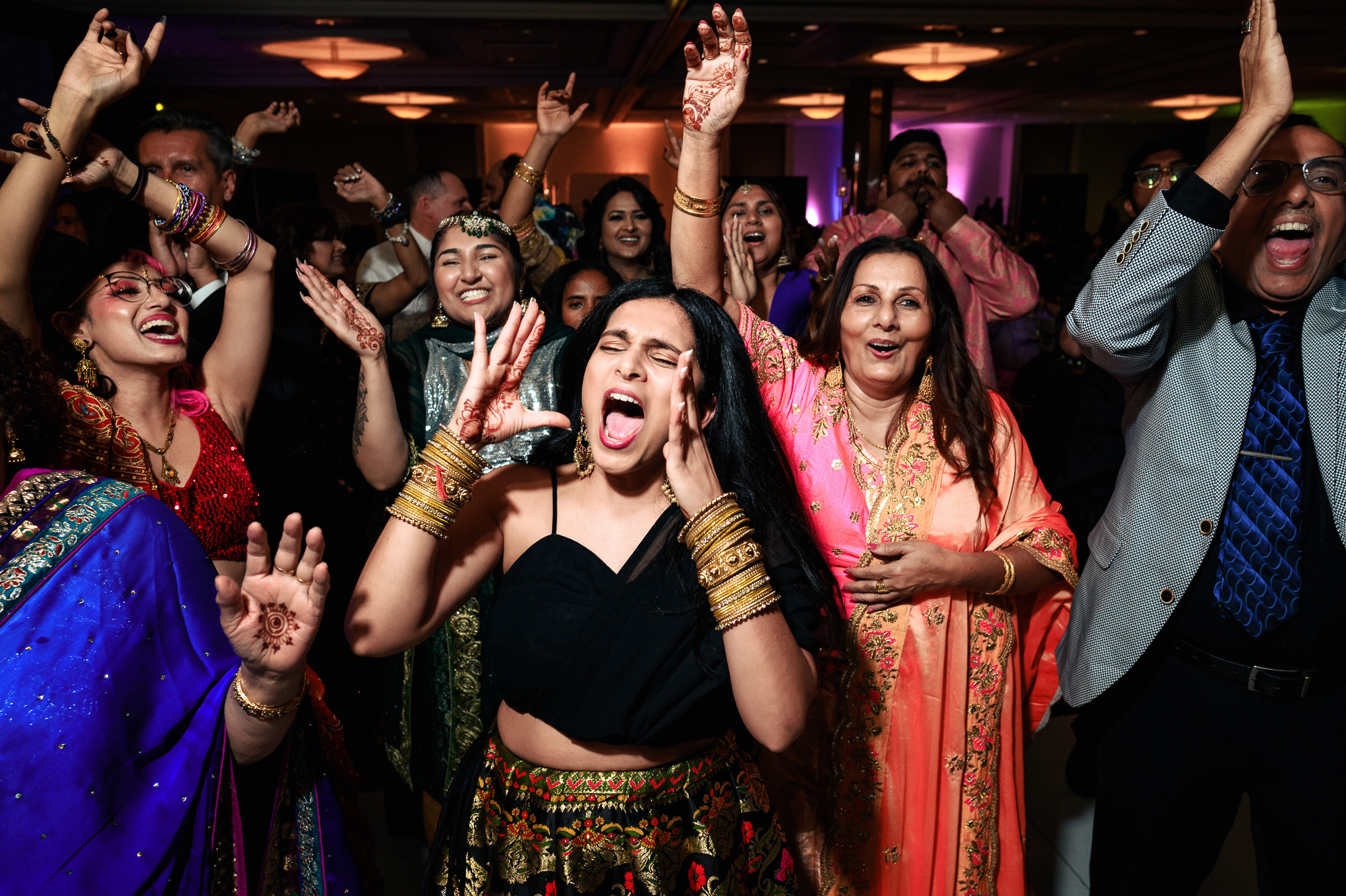 People dancing energetically at a festive event, some with hands raised and smiling.