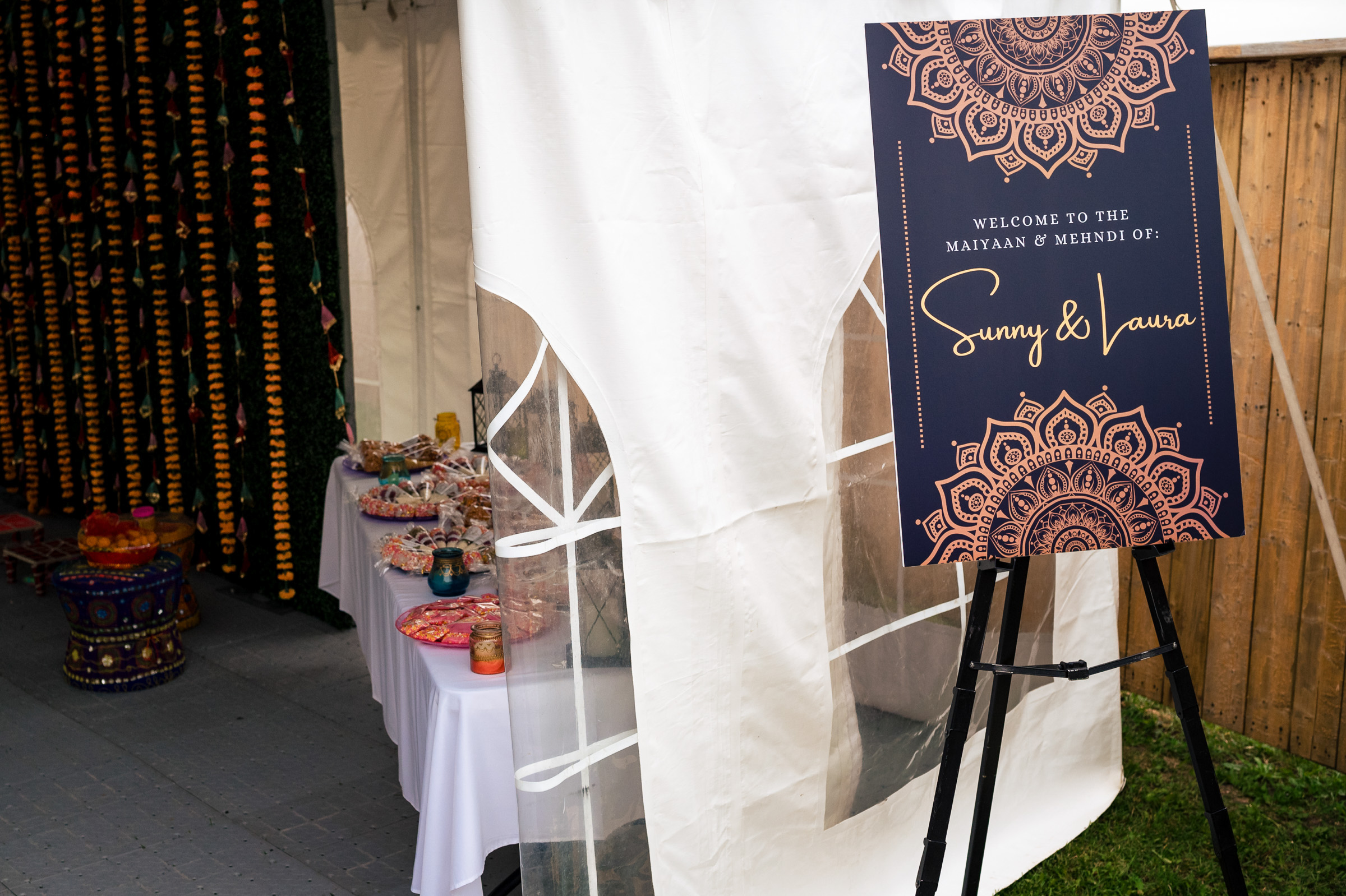 Decorated event entrance with sign: "Welcome to the Maayan & Mehendi of Sunny & Laura.