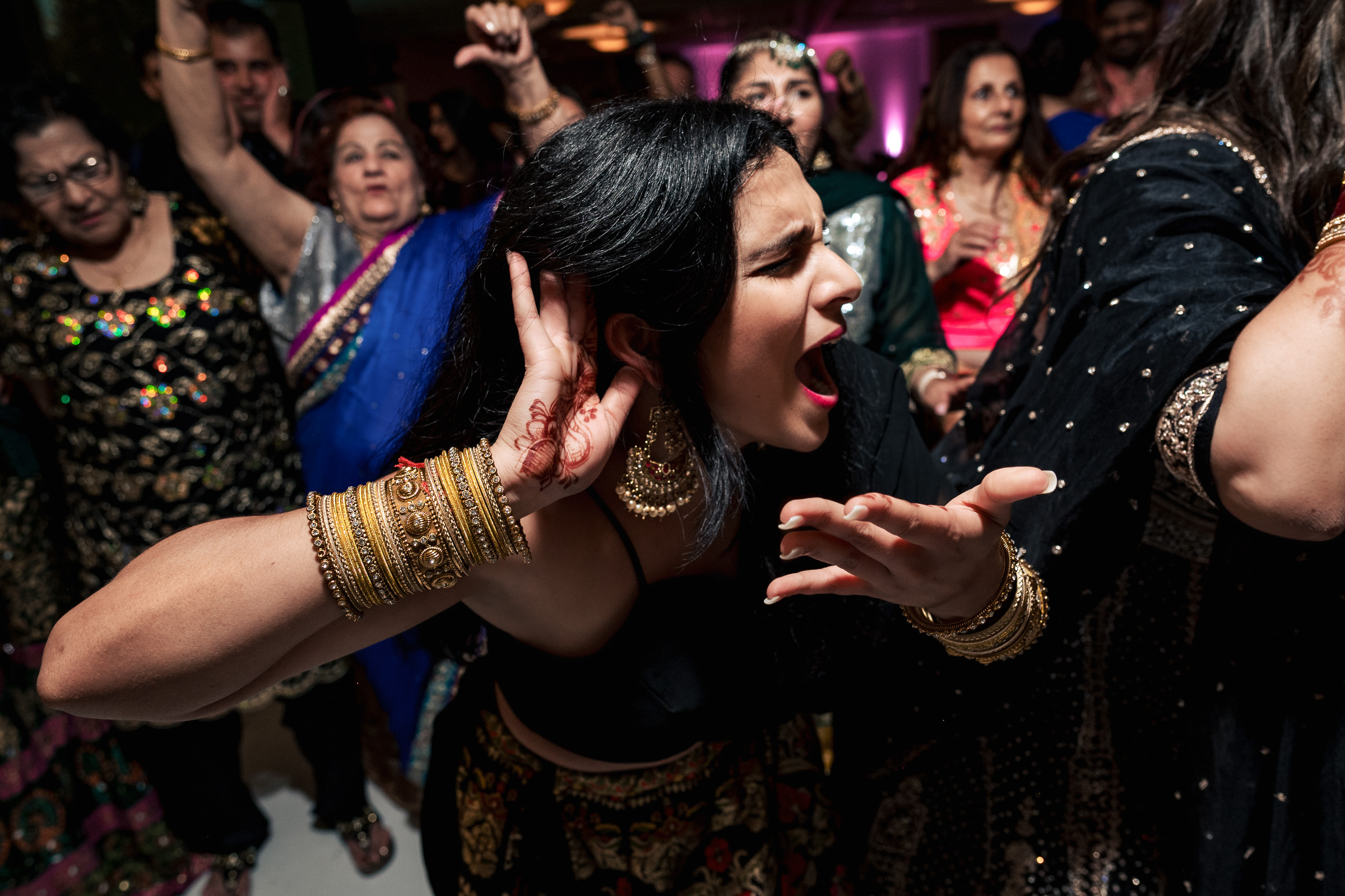 Person at a lively party, wearing traditional attire, gestures energetically amidst a crowd.