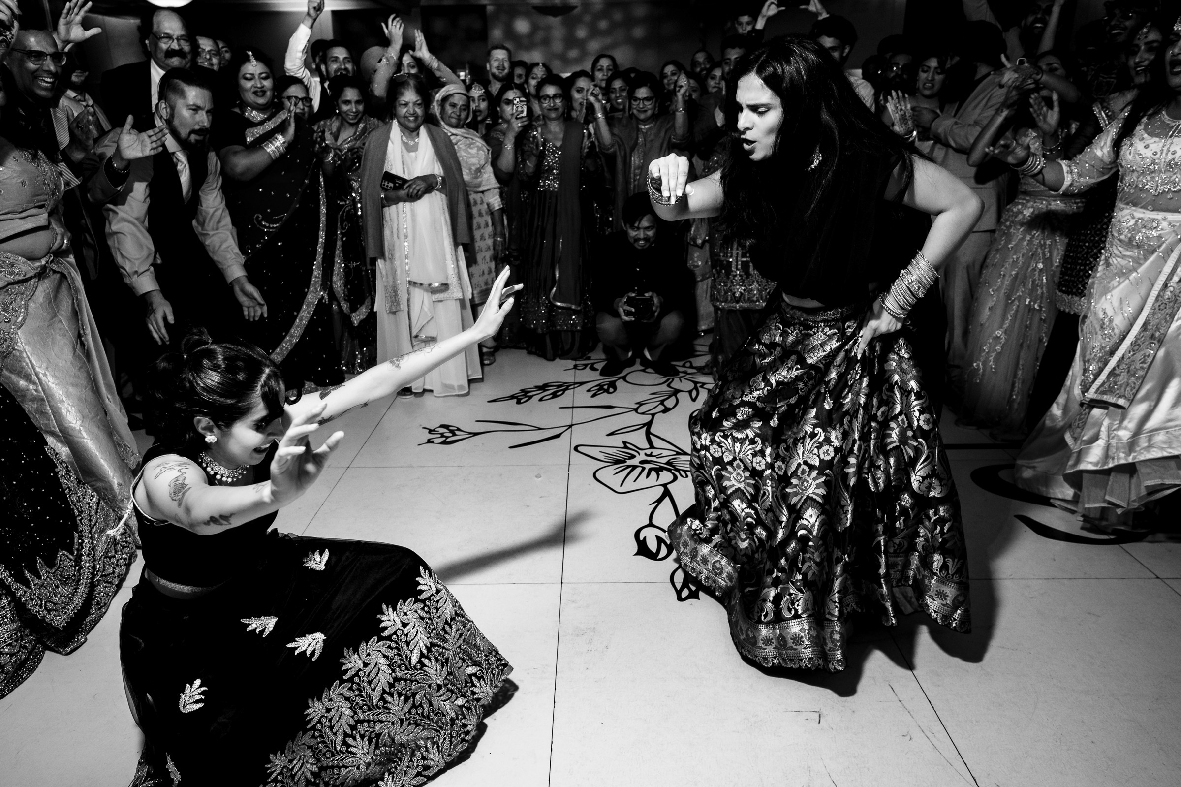 Two women dancing energetically in traditional attire, surrounded by a cheering crowd.
