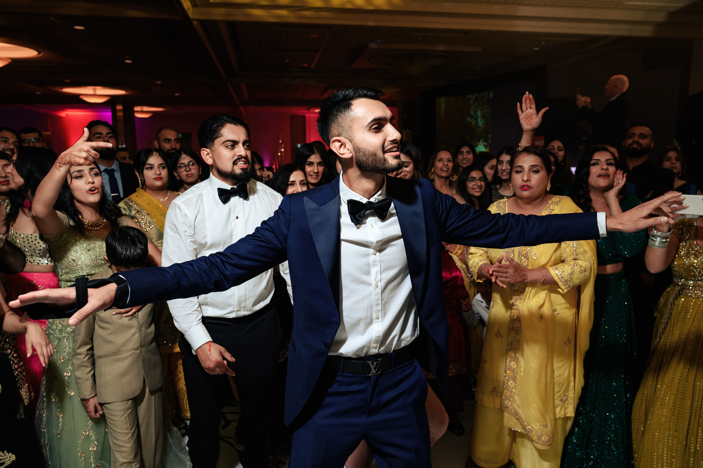 Person in a blue suit dancing joyfully at a lively party with a crowd around.