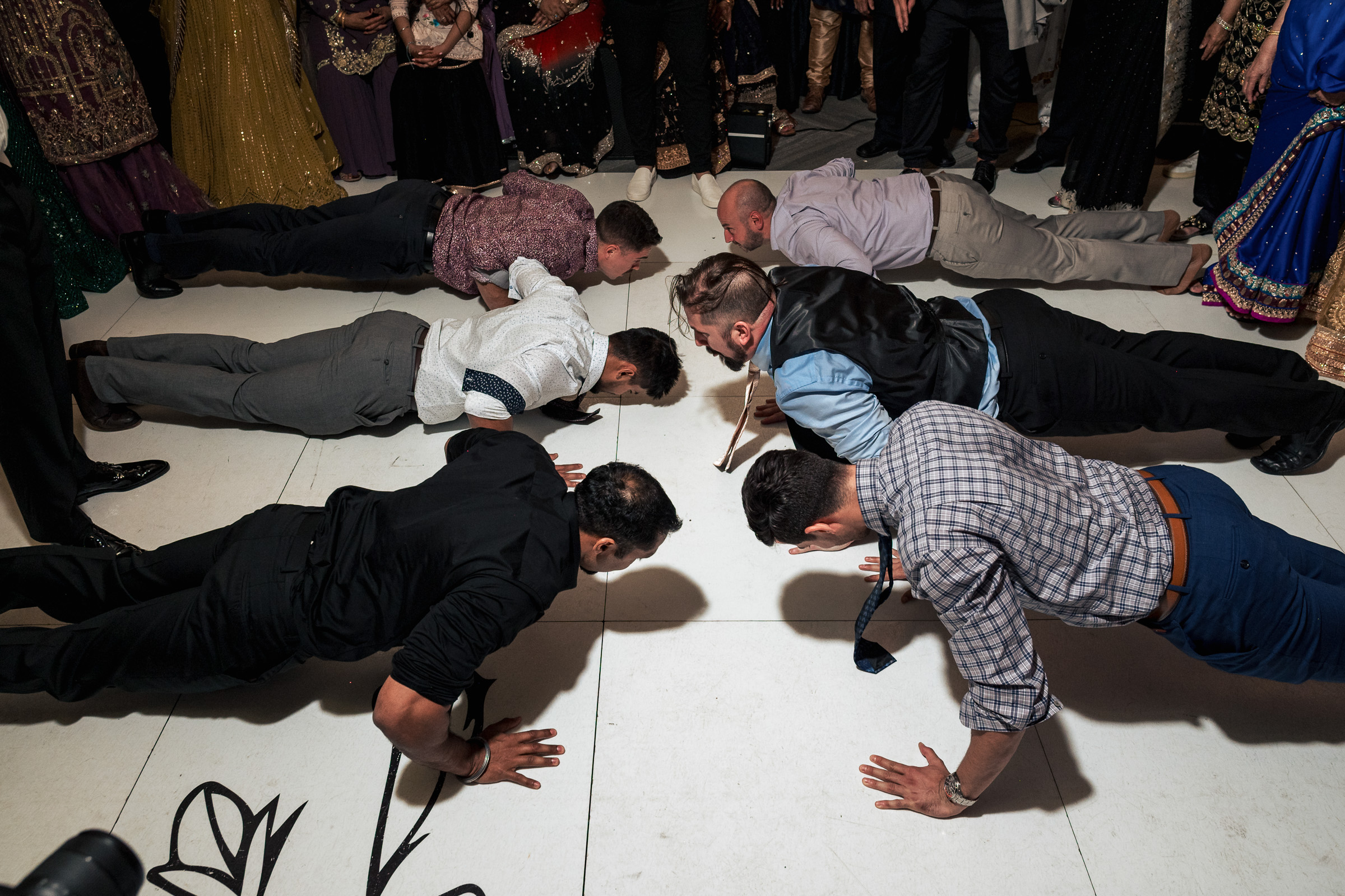 People doing push-ups on a dance floor surrounded by a group of onlookers.