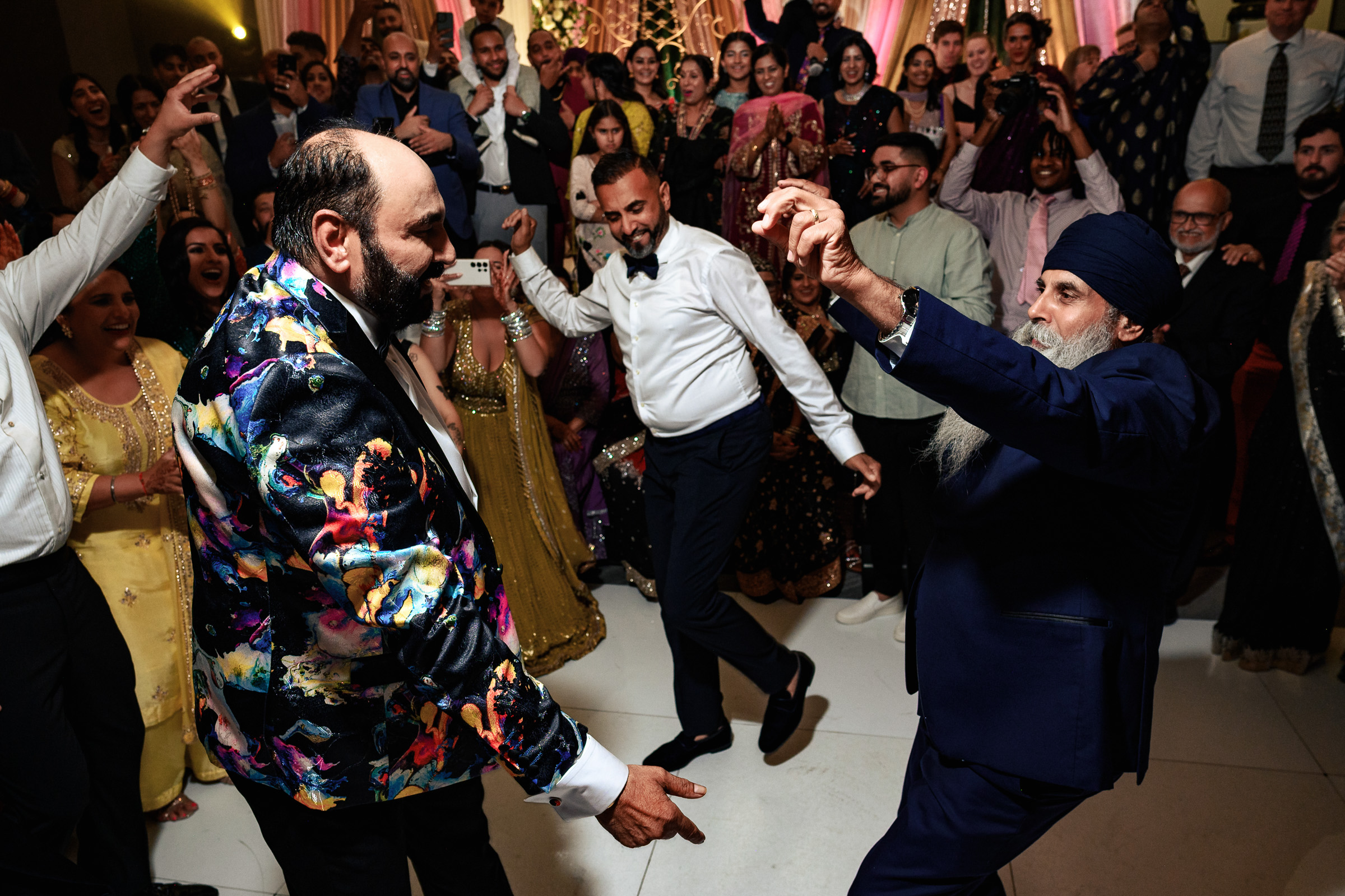 Two men dance energetically at a lively party, surrounded by cheering guests.