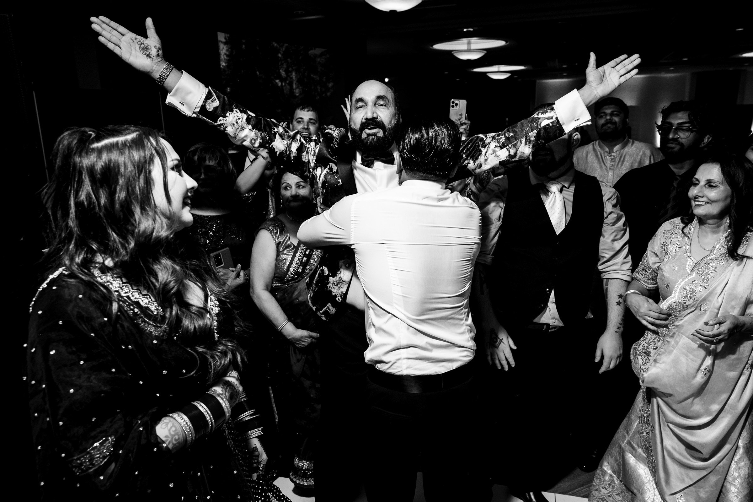 A man with outstretched arms receives a hug amid a crowd at a gathering.
