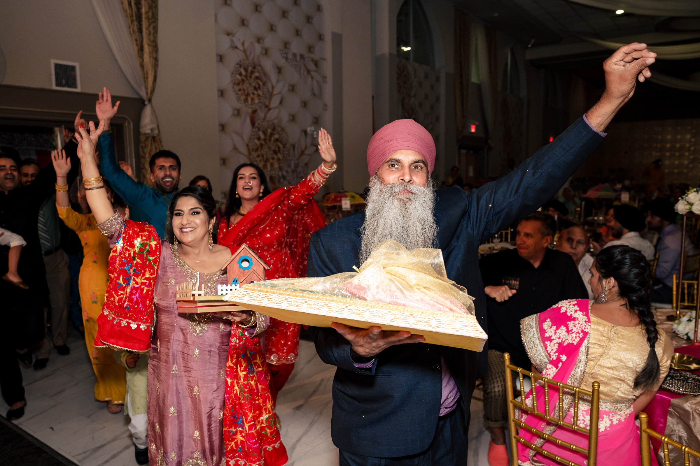 People in colorful attire dancing joyfully at an indoor celebration, holding ornaments.