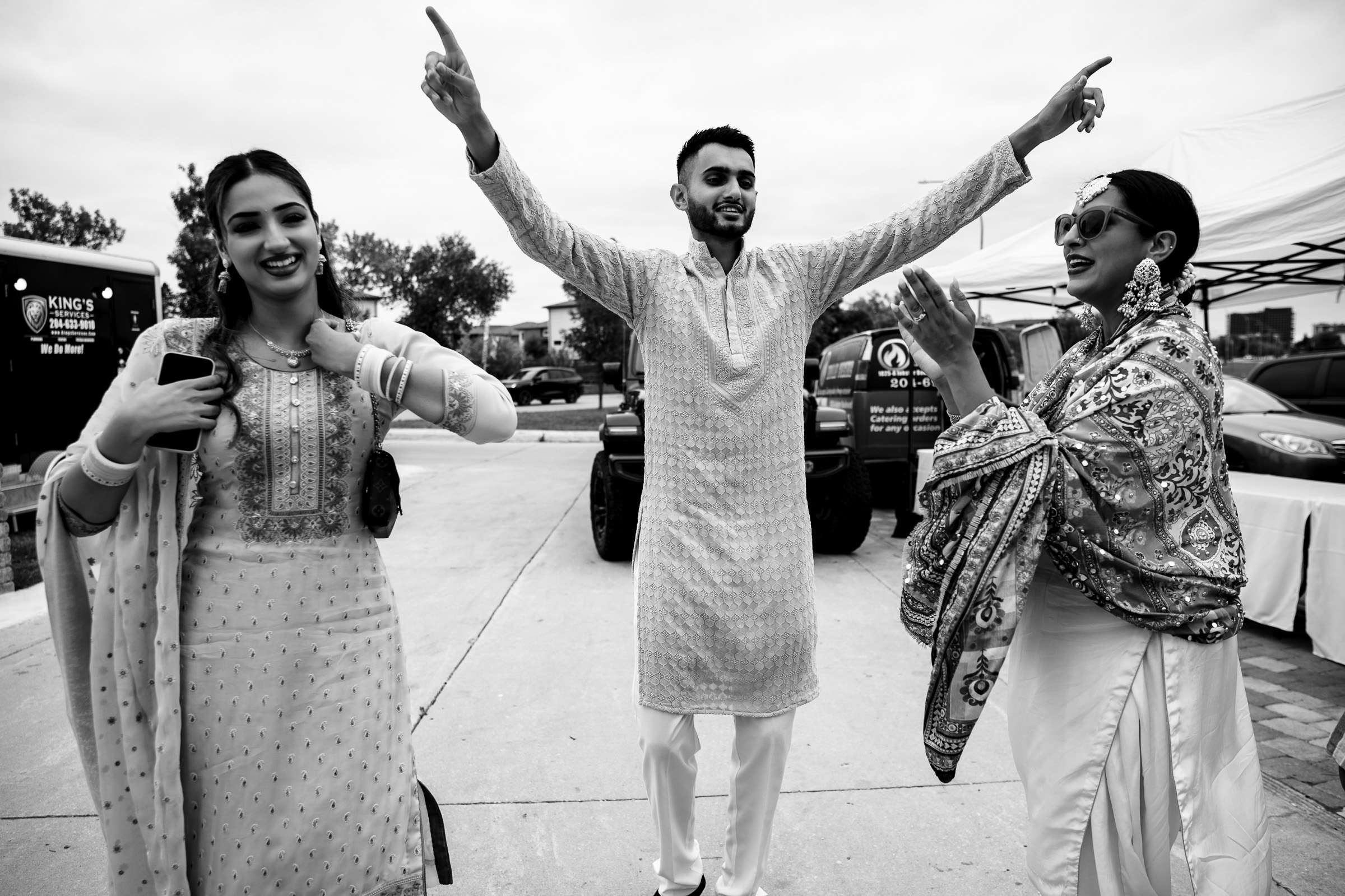 Three people in traditional attire joyfully dancing and clapping outdoors.