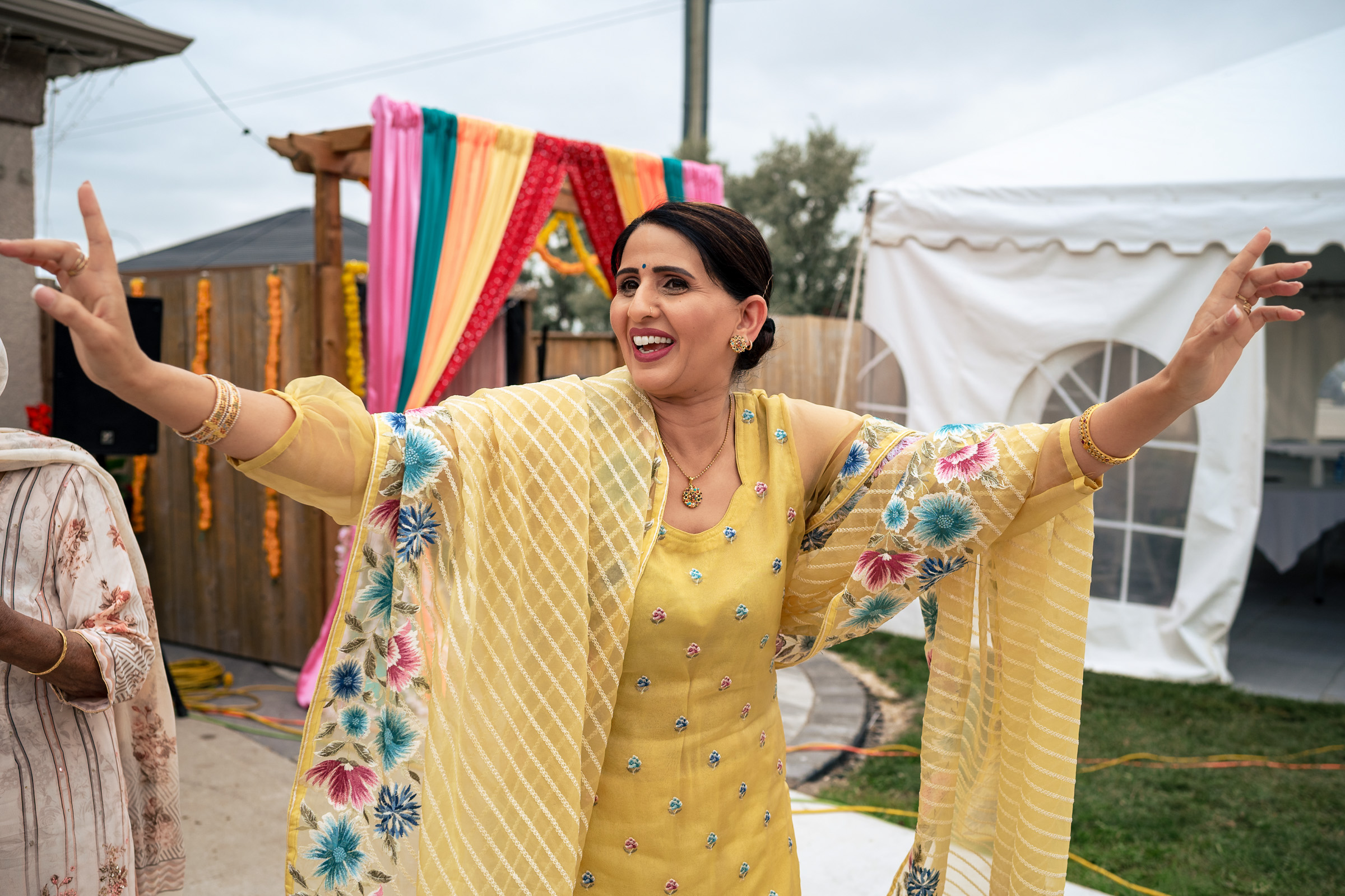 Woman in yellow outfit dancing joyfully at an outdoor cultural event.
