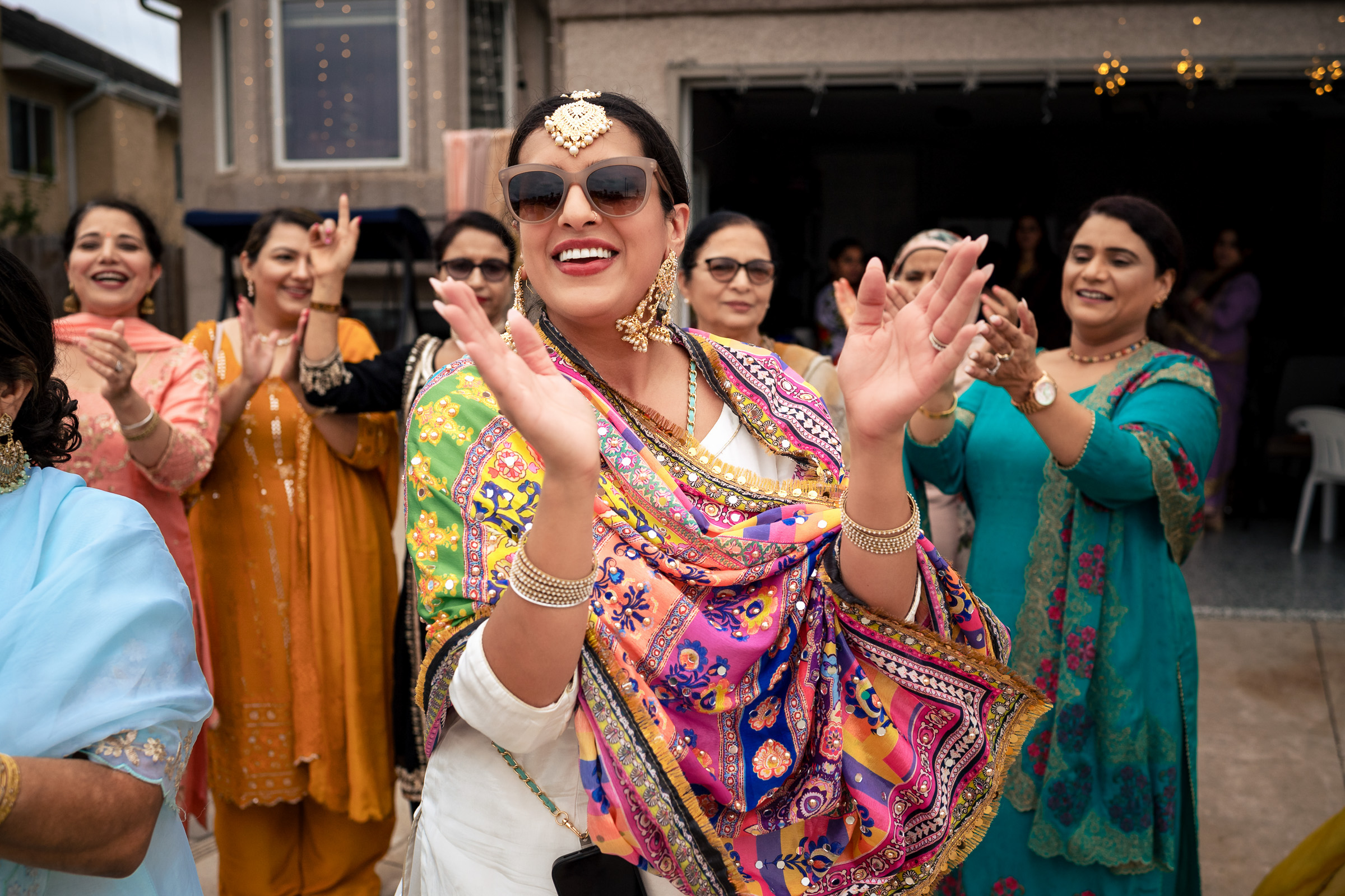 A woman in colorful traditional attire clapping joyfully with others at an outdoor gathering.