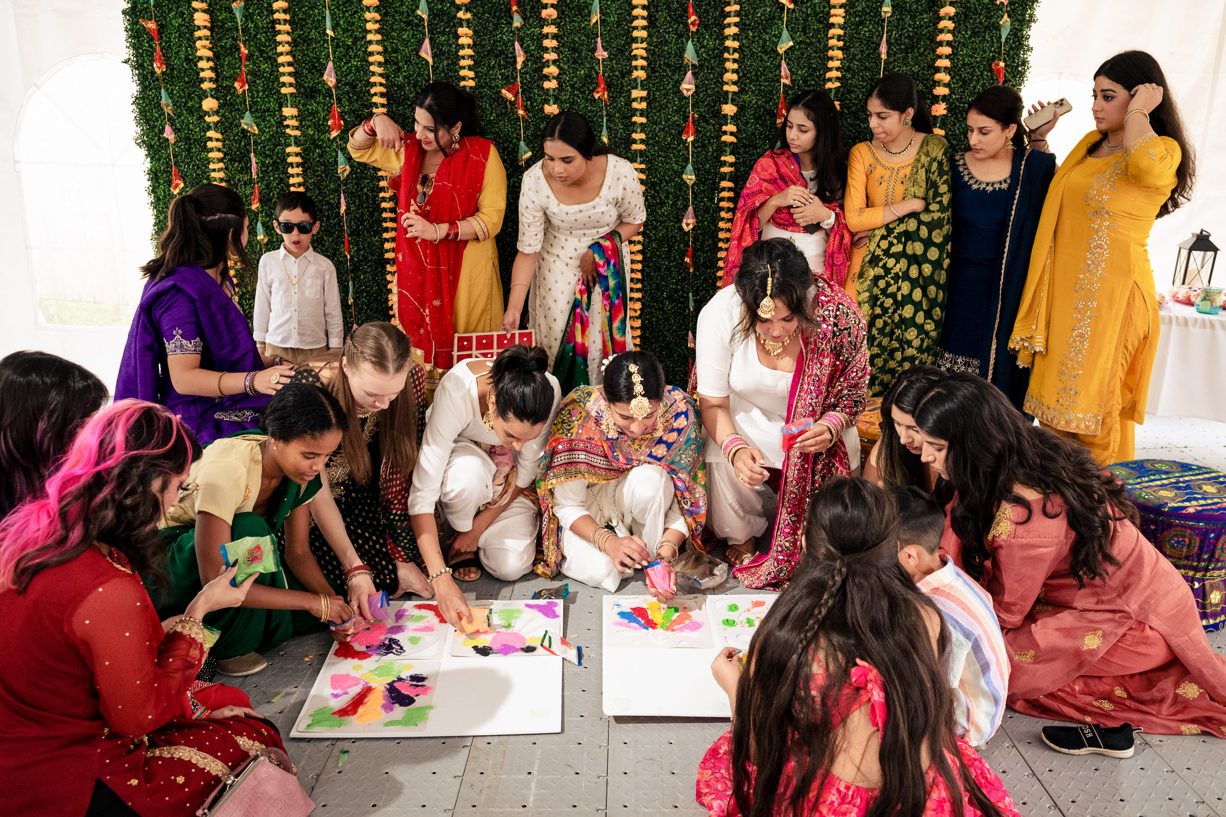 A group of people in colorful attire creating artwork on the floor at a festive gathering.