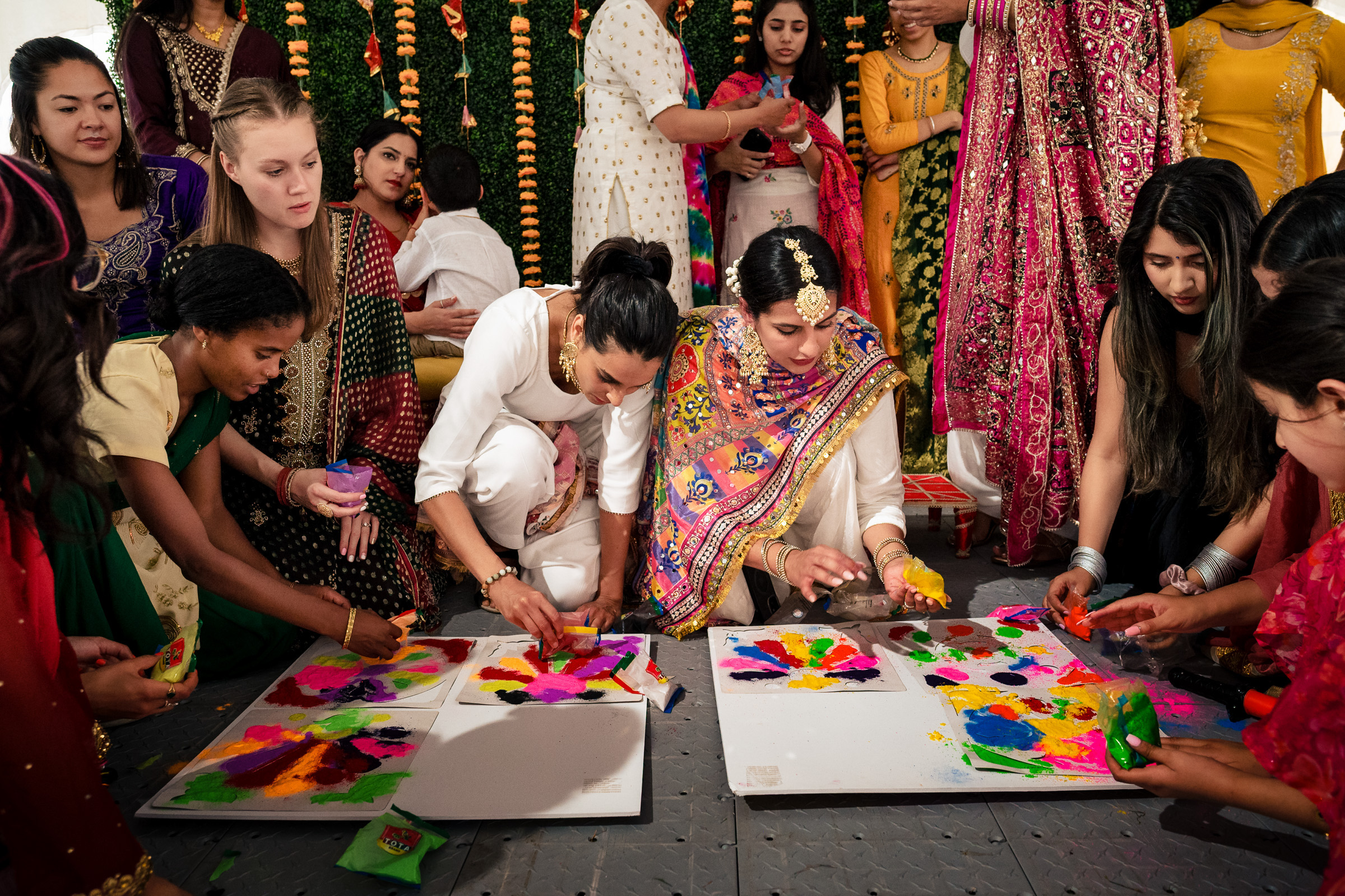Women creating colorful art on the floor at a festive gathering.