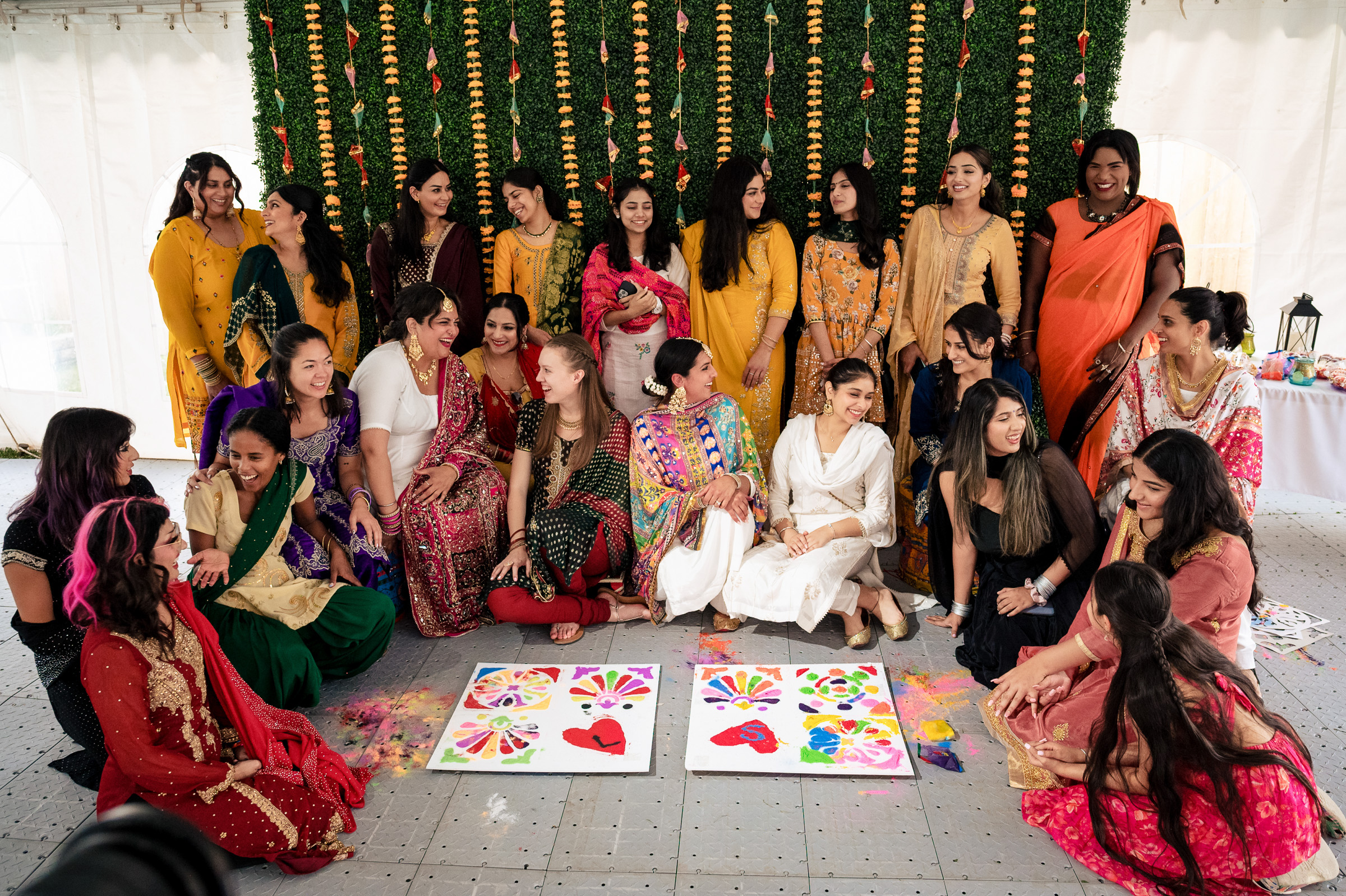 Group of women in colorful traditional attire posing with painted canvases.