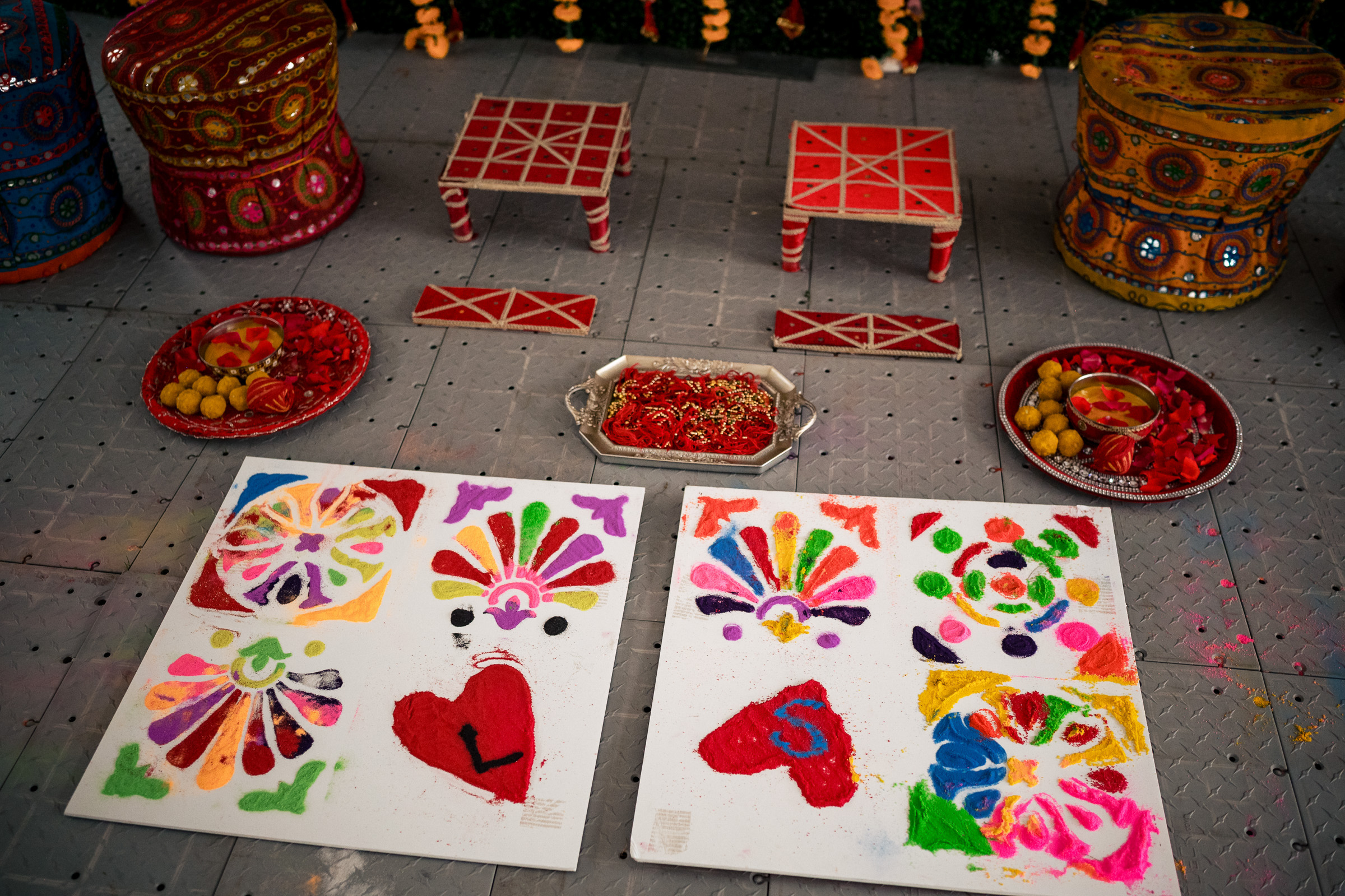 Colorful rangoli designs on the ground with decorative stools and plates of sweets nearby.