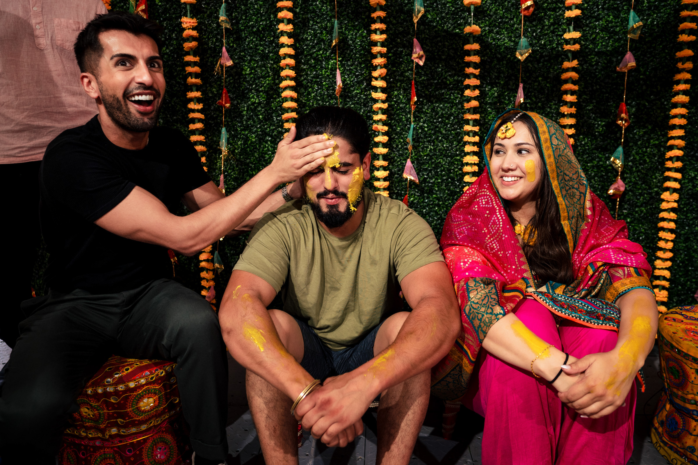 Three people celebrating with festive decorations and turmeric applied to their faces.