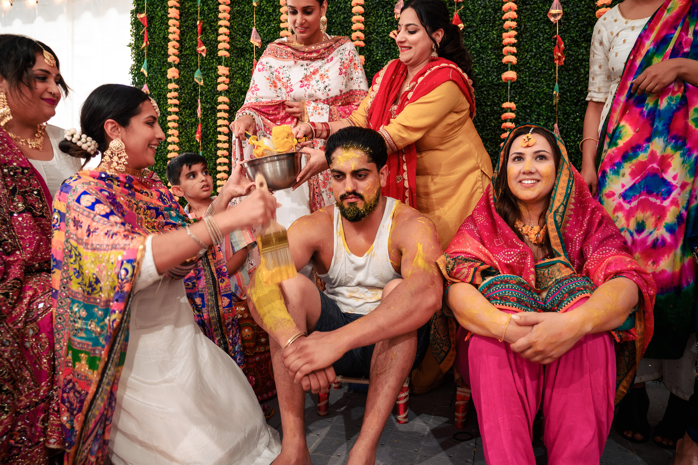 Group celebrating a traditional ceremony, applying turmeric paste on a seated man.