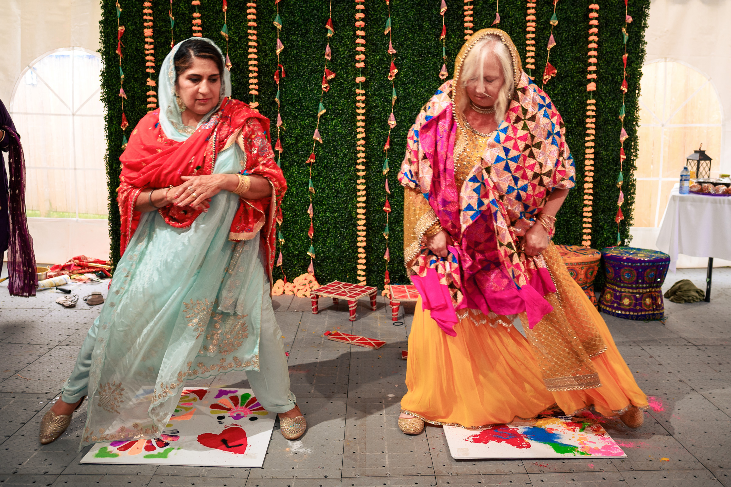 Two women step on painted canvases at a colorful outdoor event.