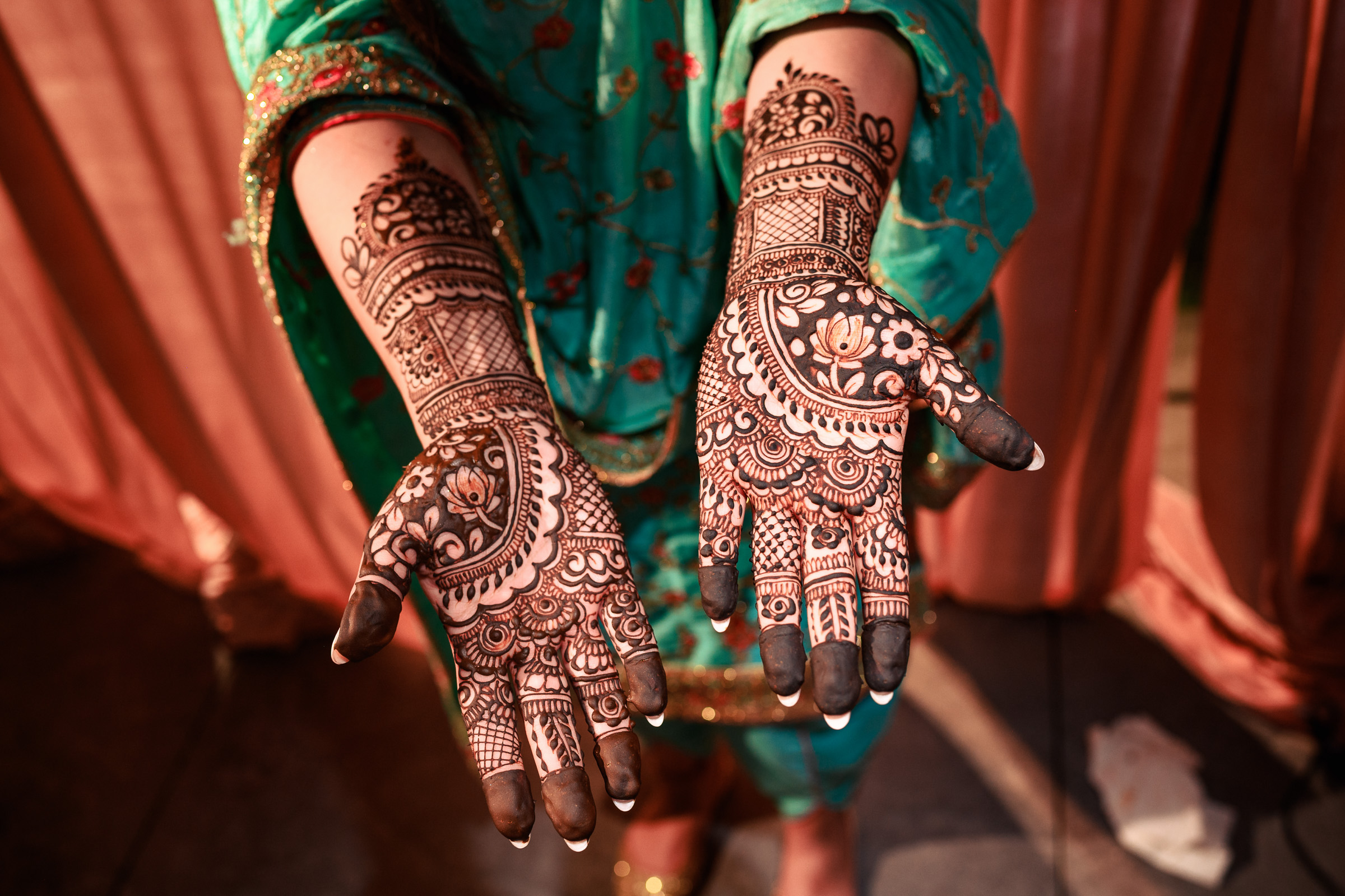Hands with intricate henna designs, wearing a teal garment.