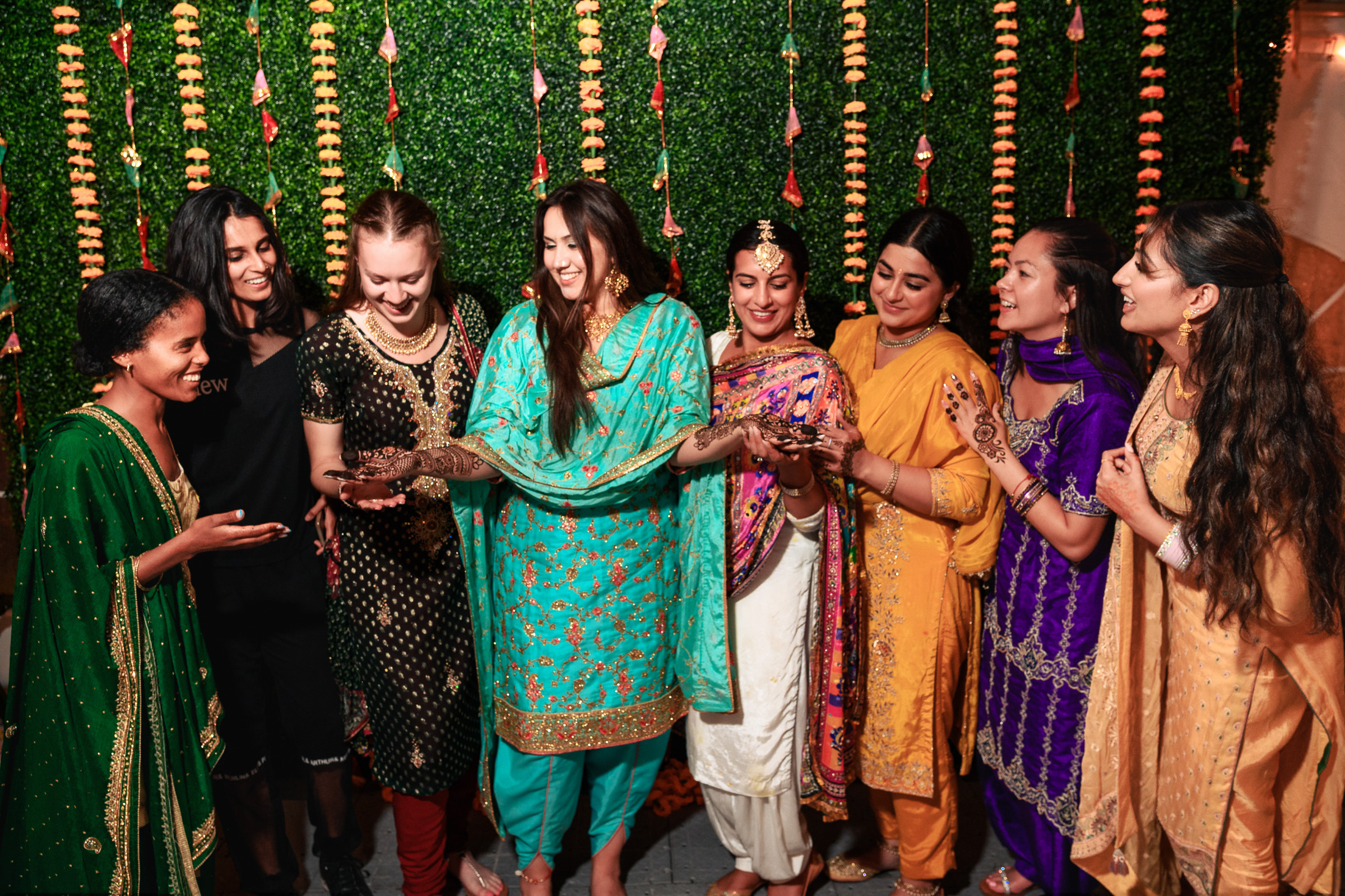 A group of women in vibrant traditional attire, smiling and showing henna on their hands.