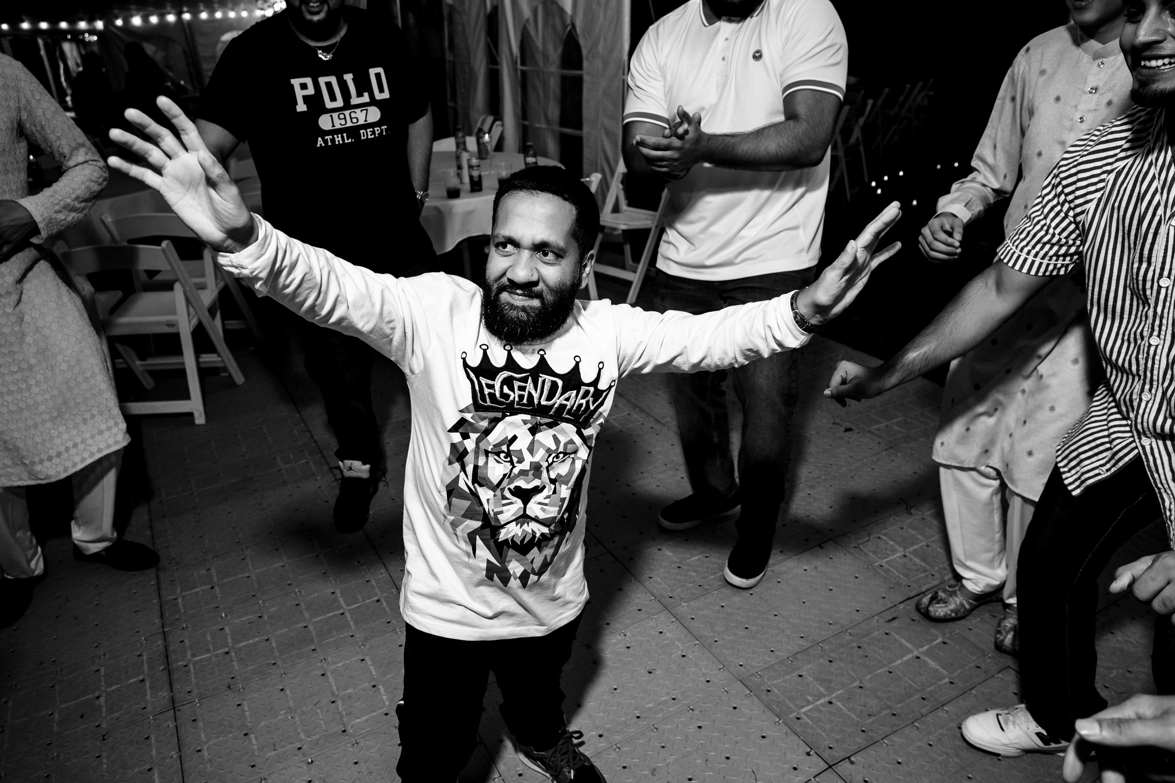 Person dancing energetically with a lion graphic on shirt, surrounded by others clapping.