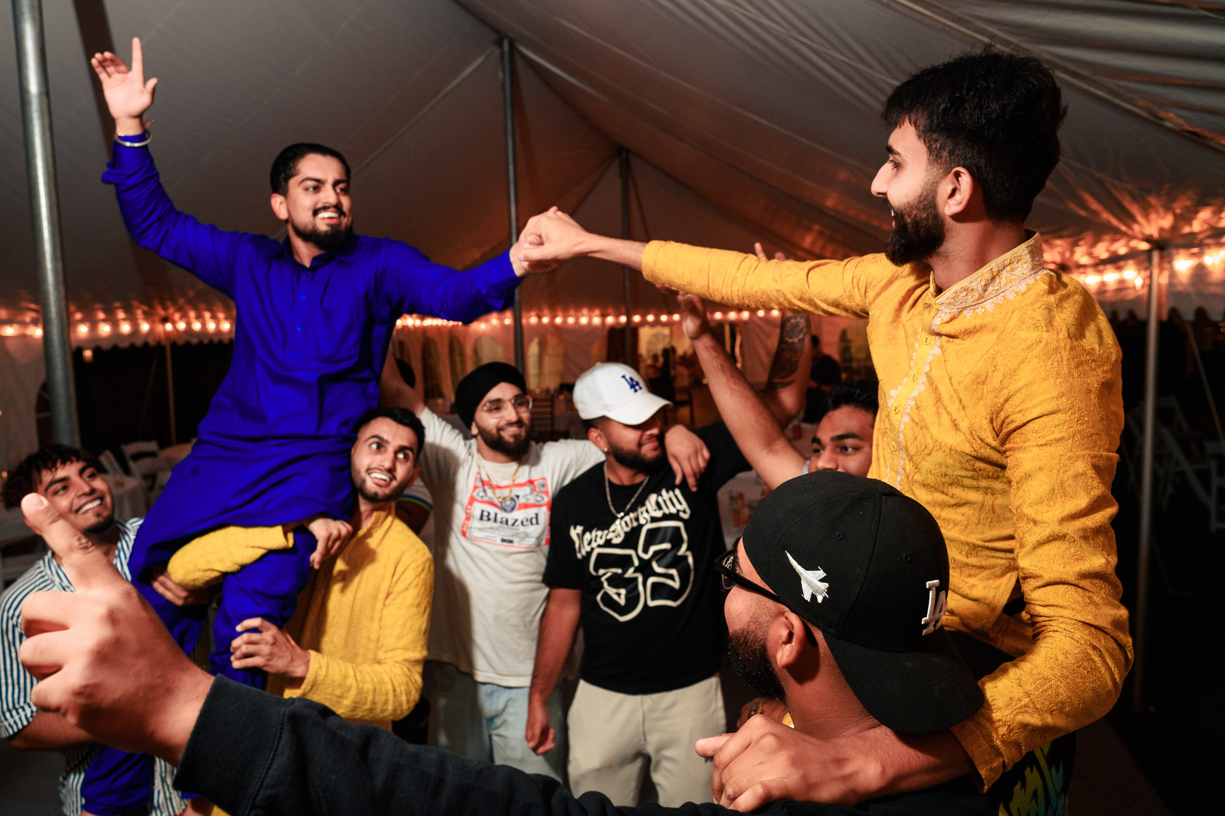 Group of men celebrating under a tent with some lifting others on their shoulders.