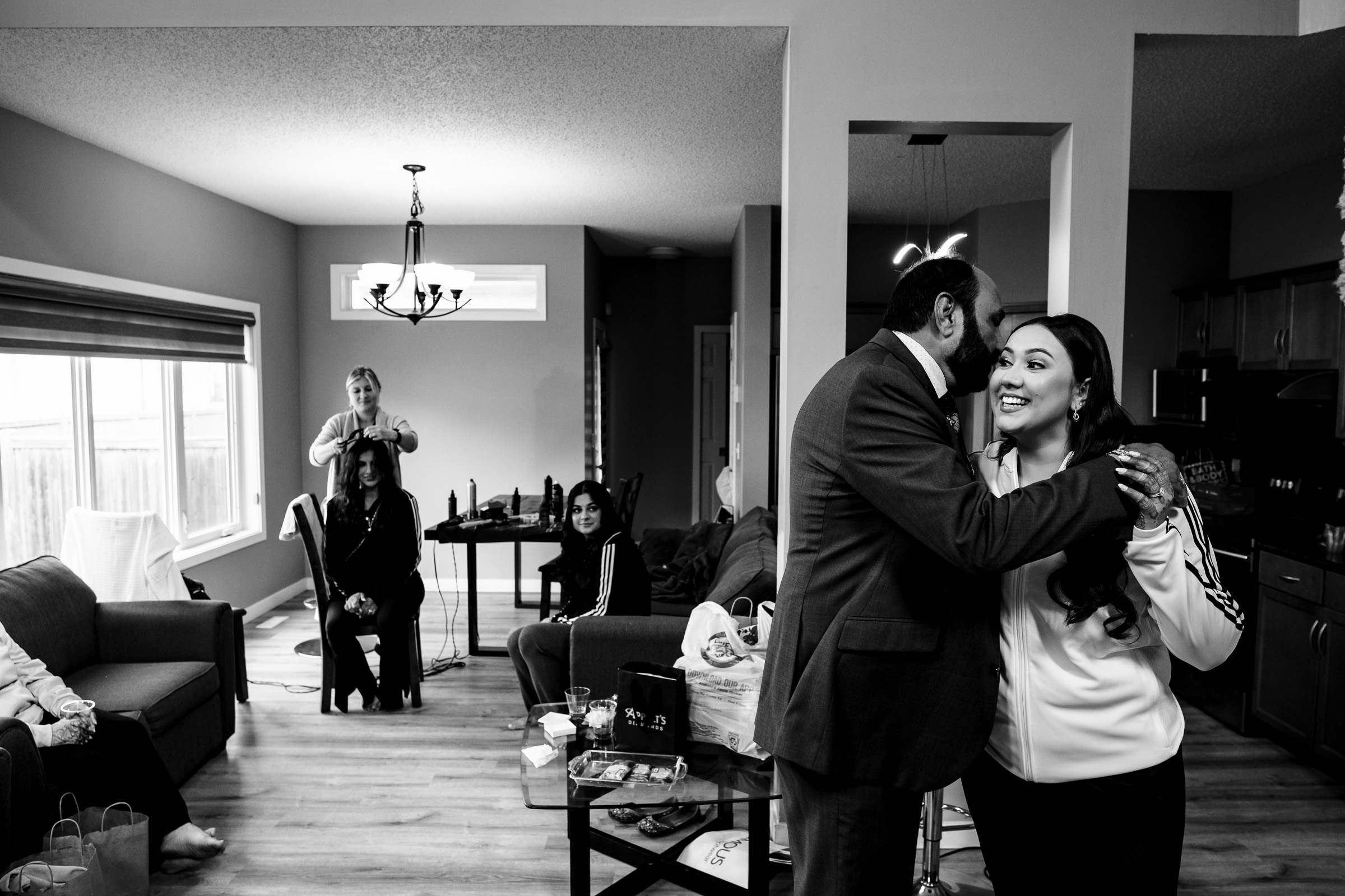 People in a living room, man hugging woman, others seated and standing in background.