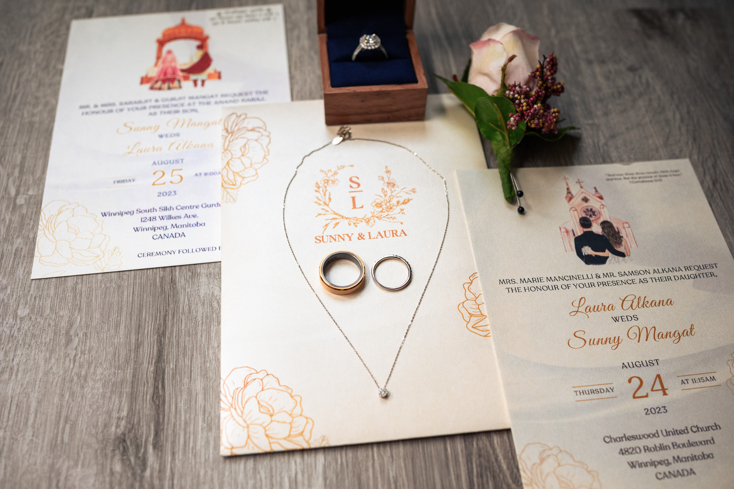 Wedding invitations, rings, necklace, and floral boutonniere displayed on a wooden surface.